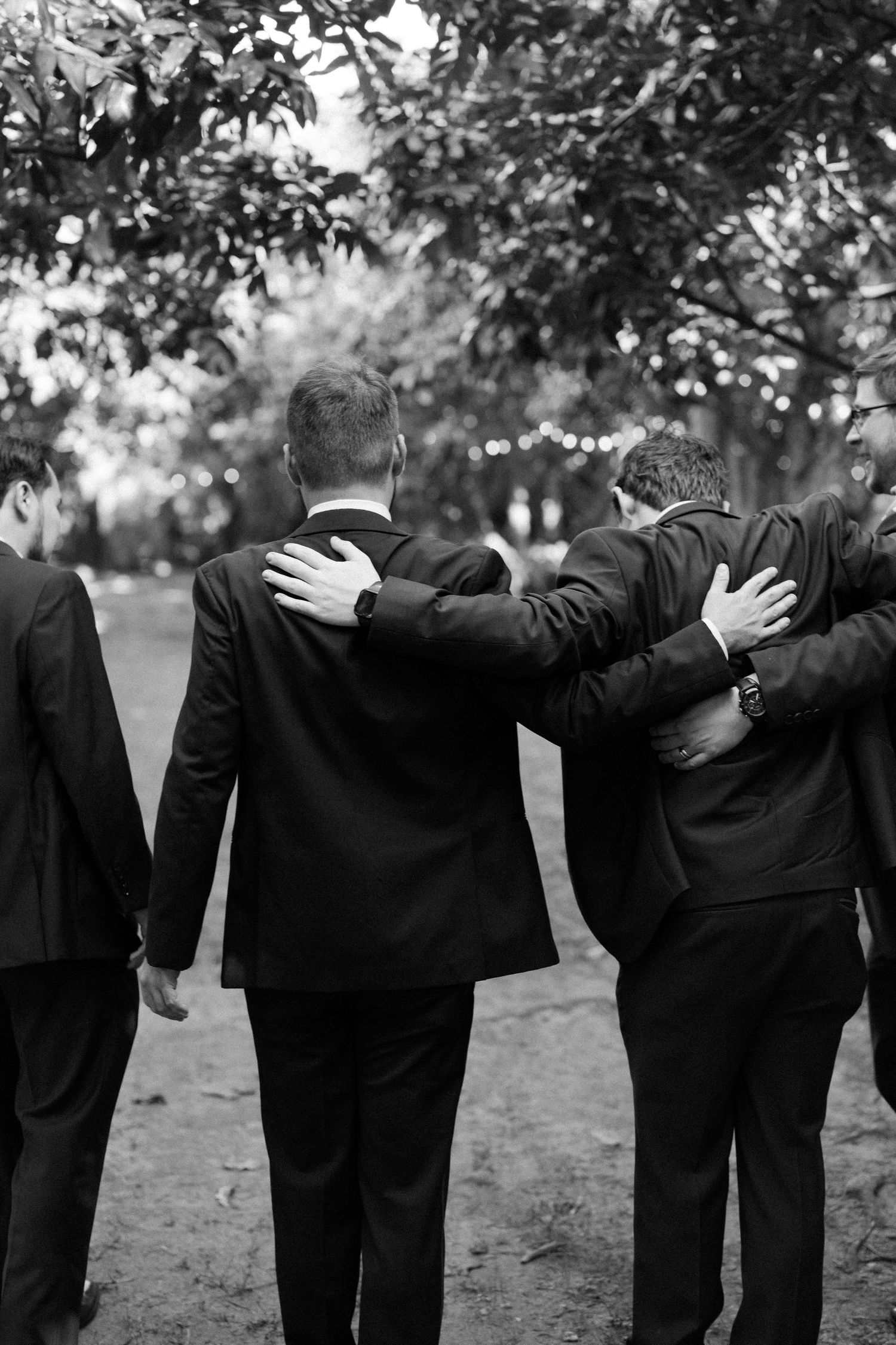 A group of men in suits embracing each other in a garden setting.