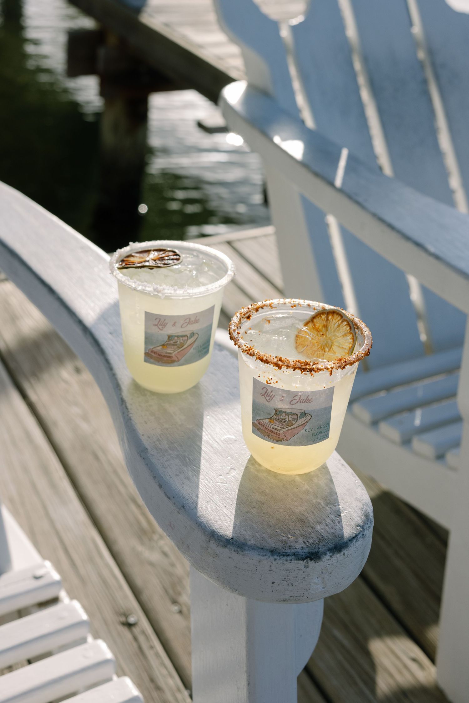 Two glasses of lemonade or iced tea sit on a wooden patio chair on a sunny day.