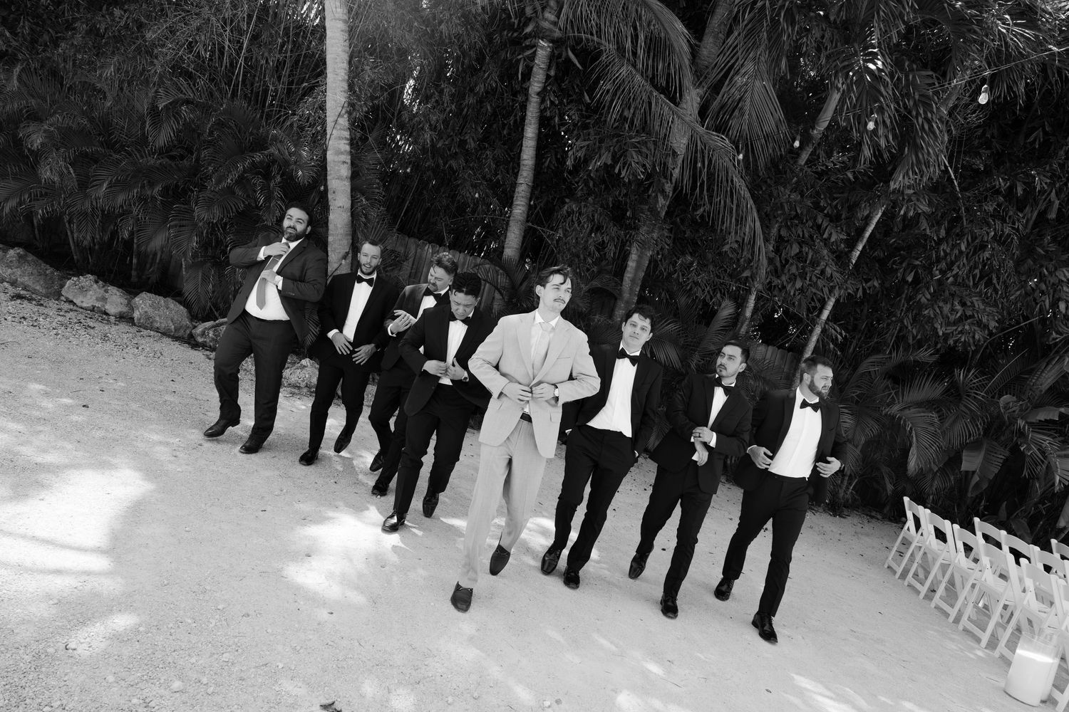 A group of men dressed in formal attire standing together in a tropical outdoor setting.