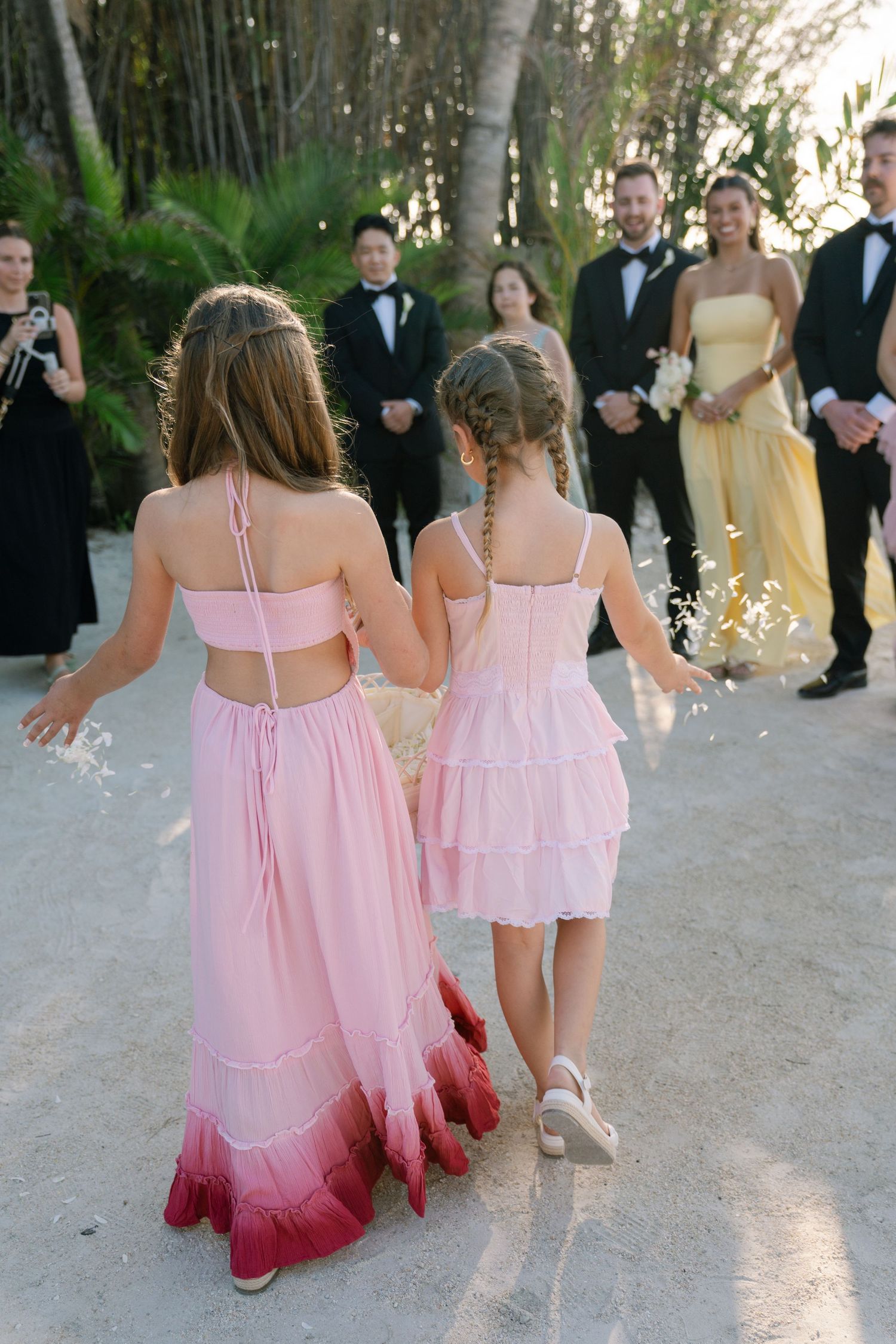 Two women in pink dresses walk together in a formal setting with other guests.