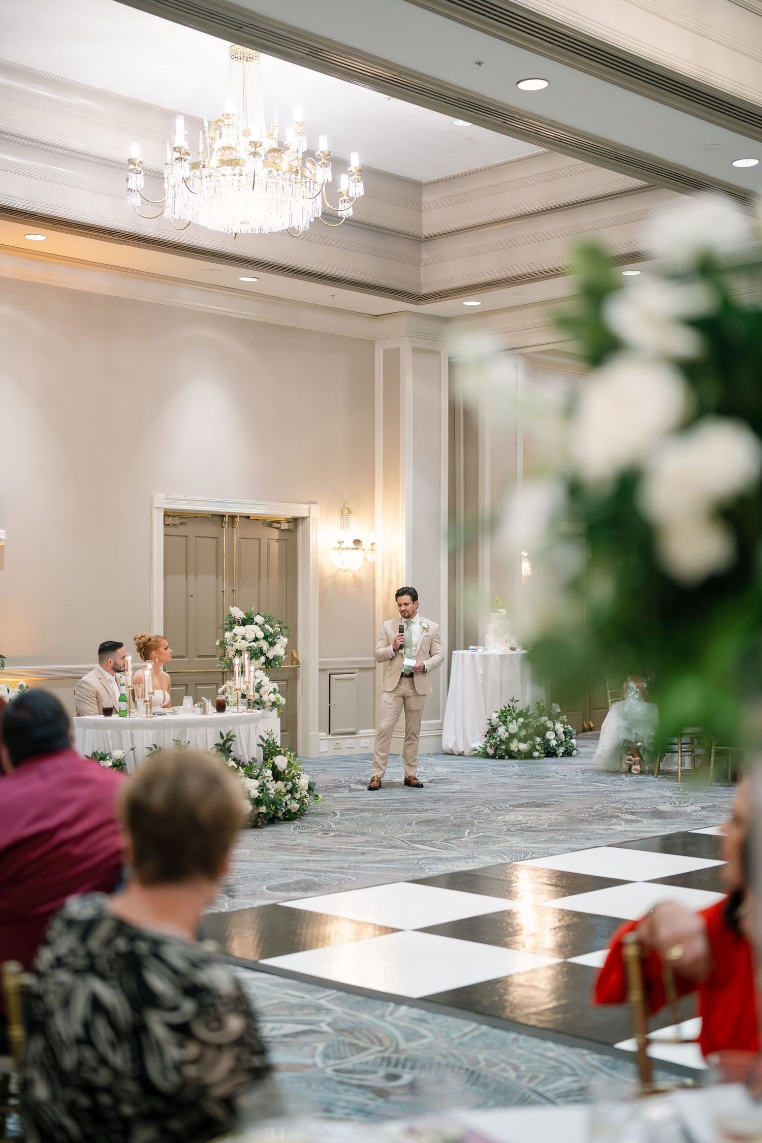 Elegant ballroom with chandeliers and white floral arrangements set up for a wedding reception.