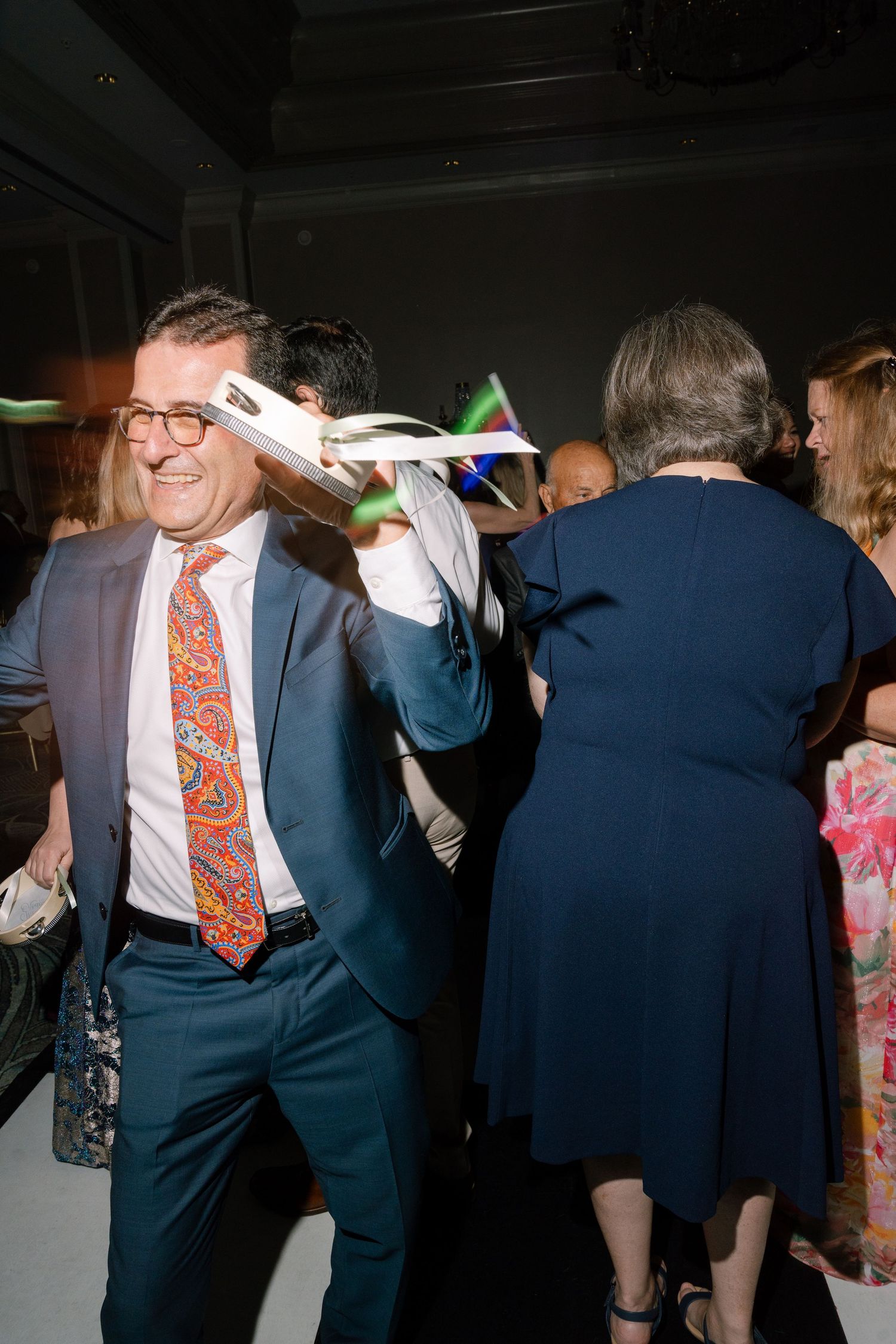 Wedding reception guests dancing in formal attire under dim lighting.