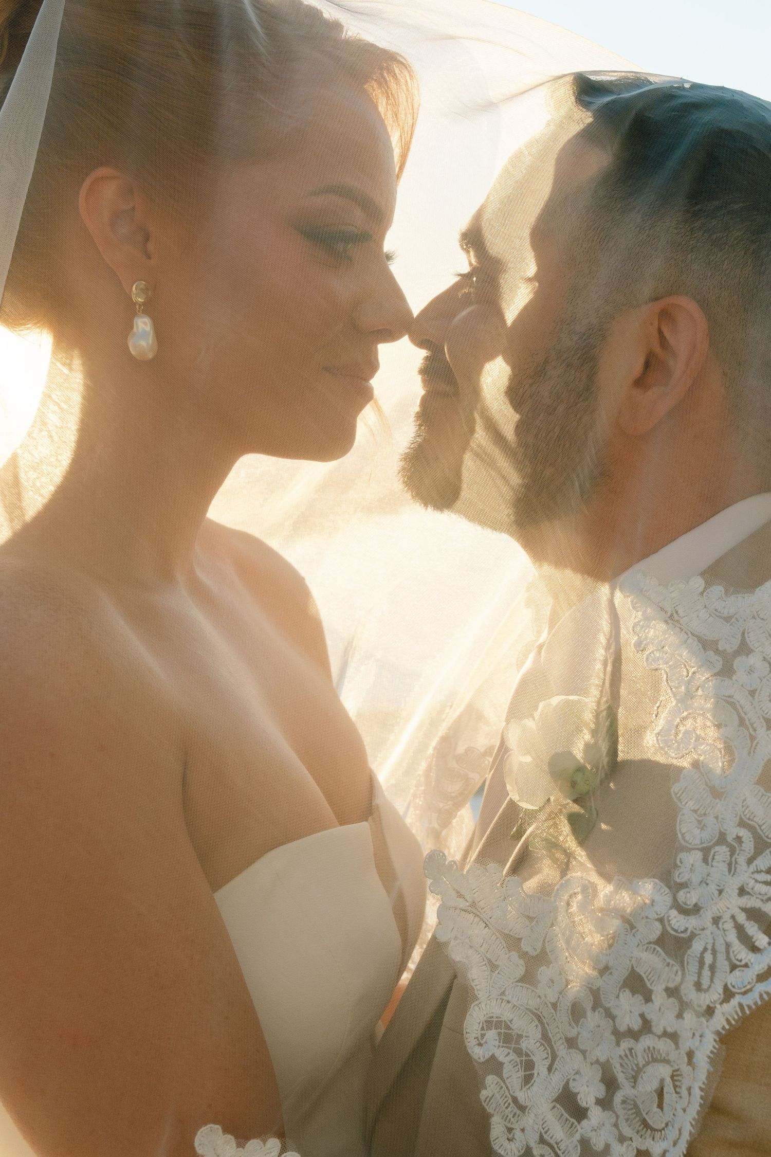 Romantic sunlit wedding couple sharing an intimate moment against a bright background.