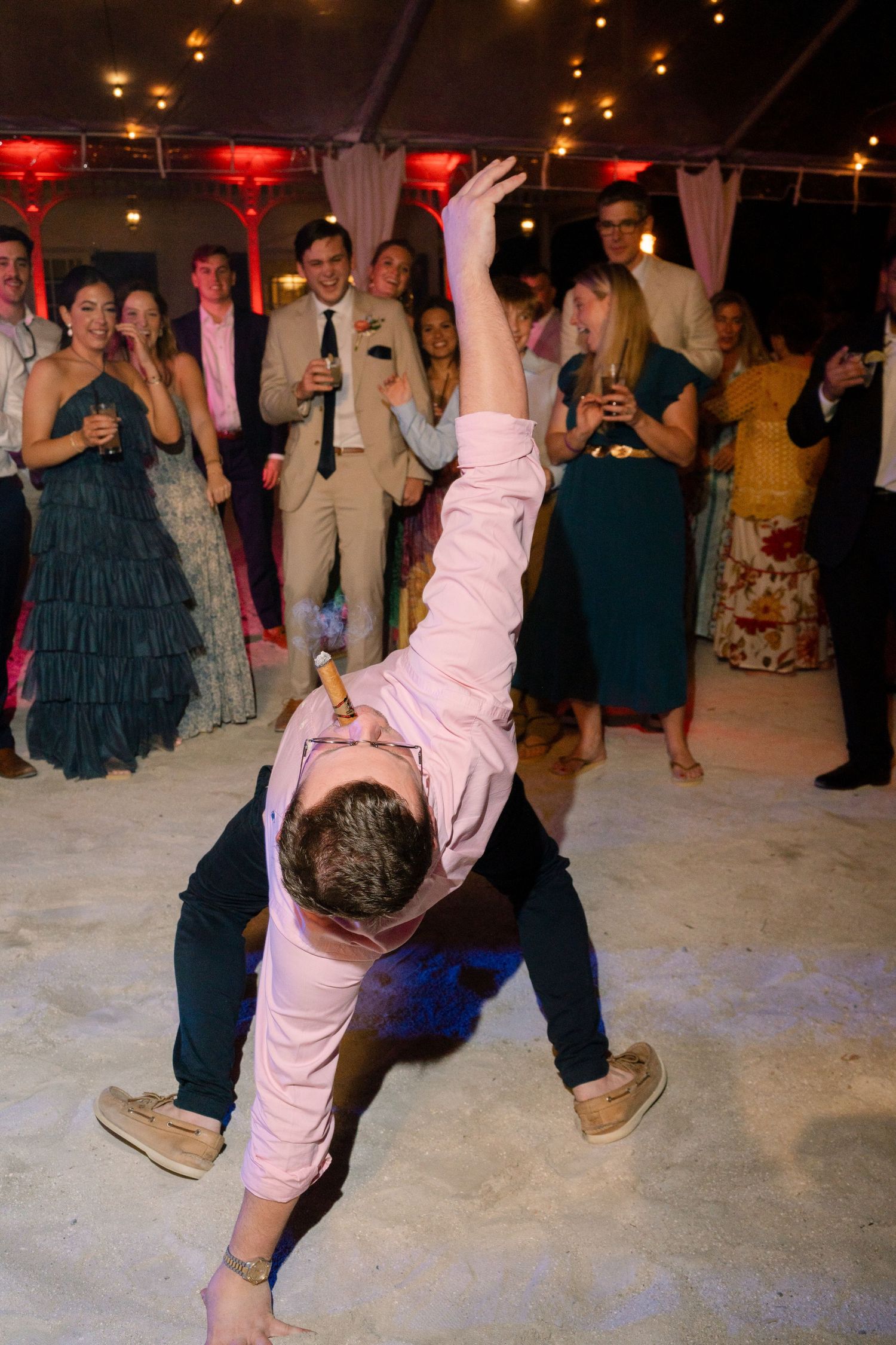 Wedding guest performs an energetic dance move in a pink shirt at the reception.