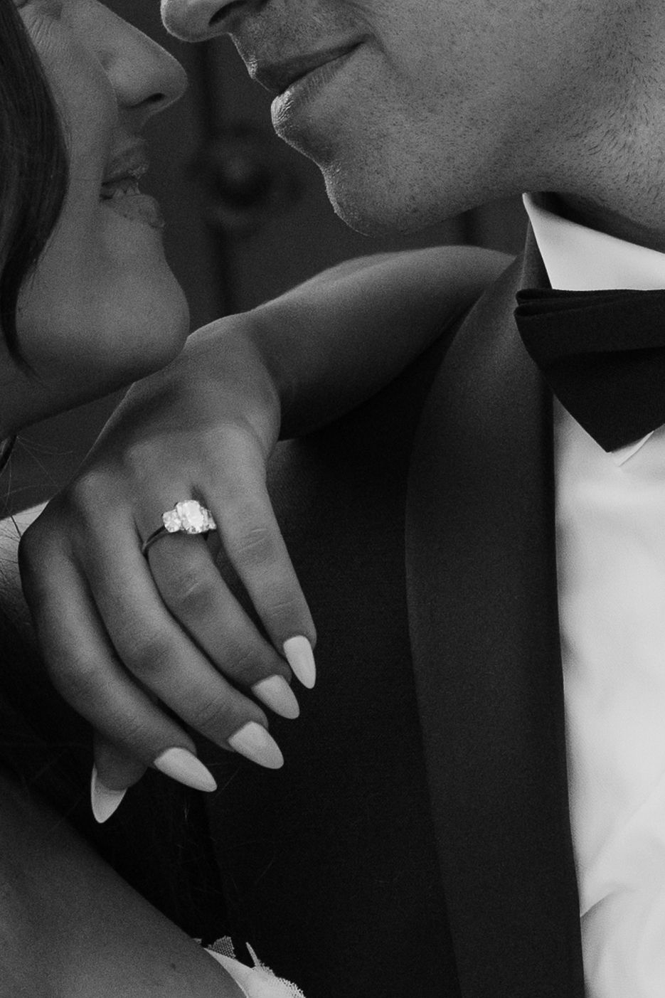 Black and white photo of bride and groom almost kissing, showcasing a stunning three-stone diamond engagement ring.