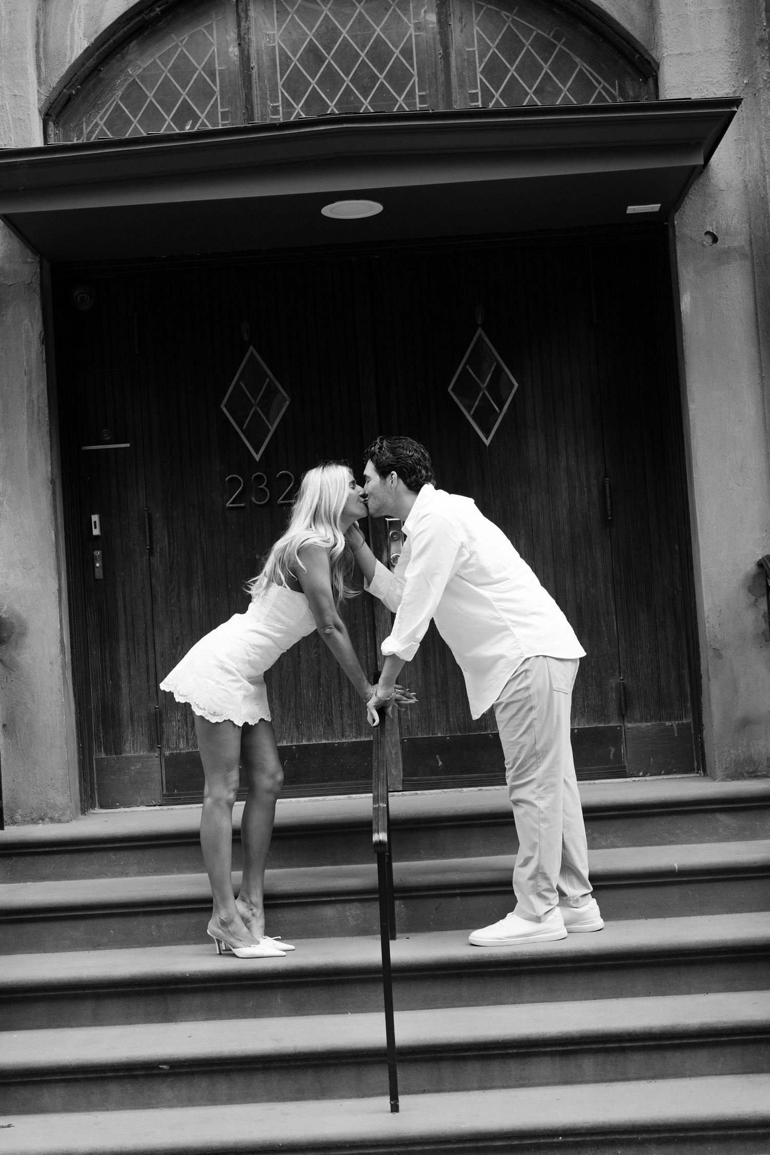 Couple sharing a kiss on steps of a historic building entrance in black and white photo.