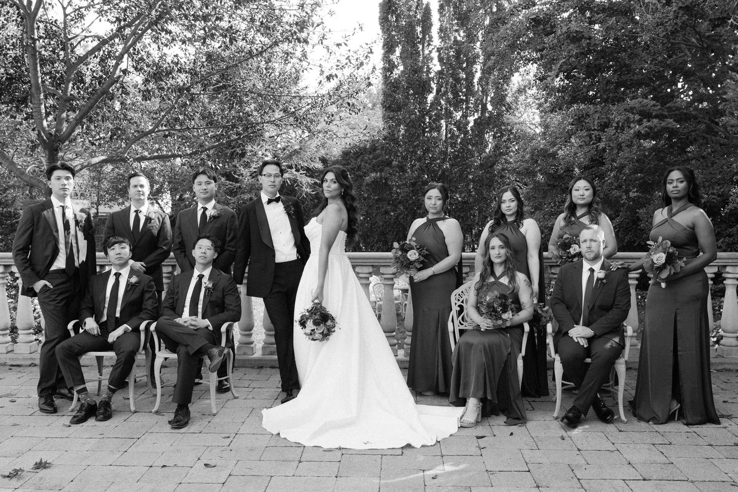 Wedding party poses for group photos outdoors in formal attire with trees in background.