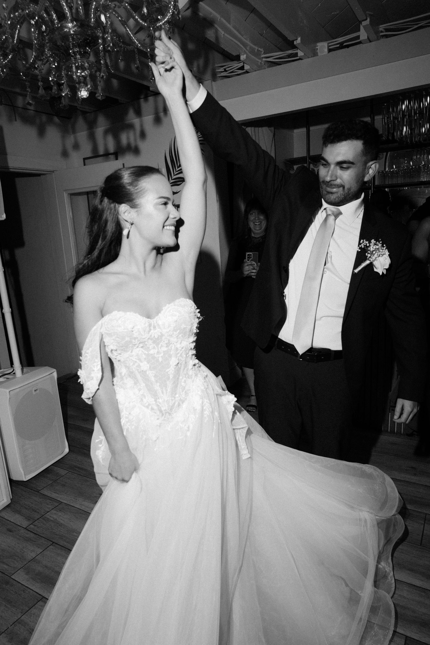 Black and white photo of bride and groom sharing first dance, groom spinning bride in elegant wedding gown.