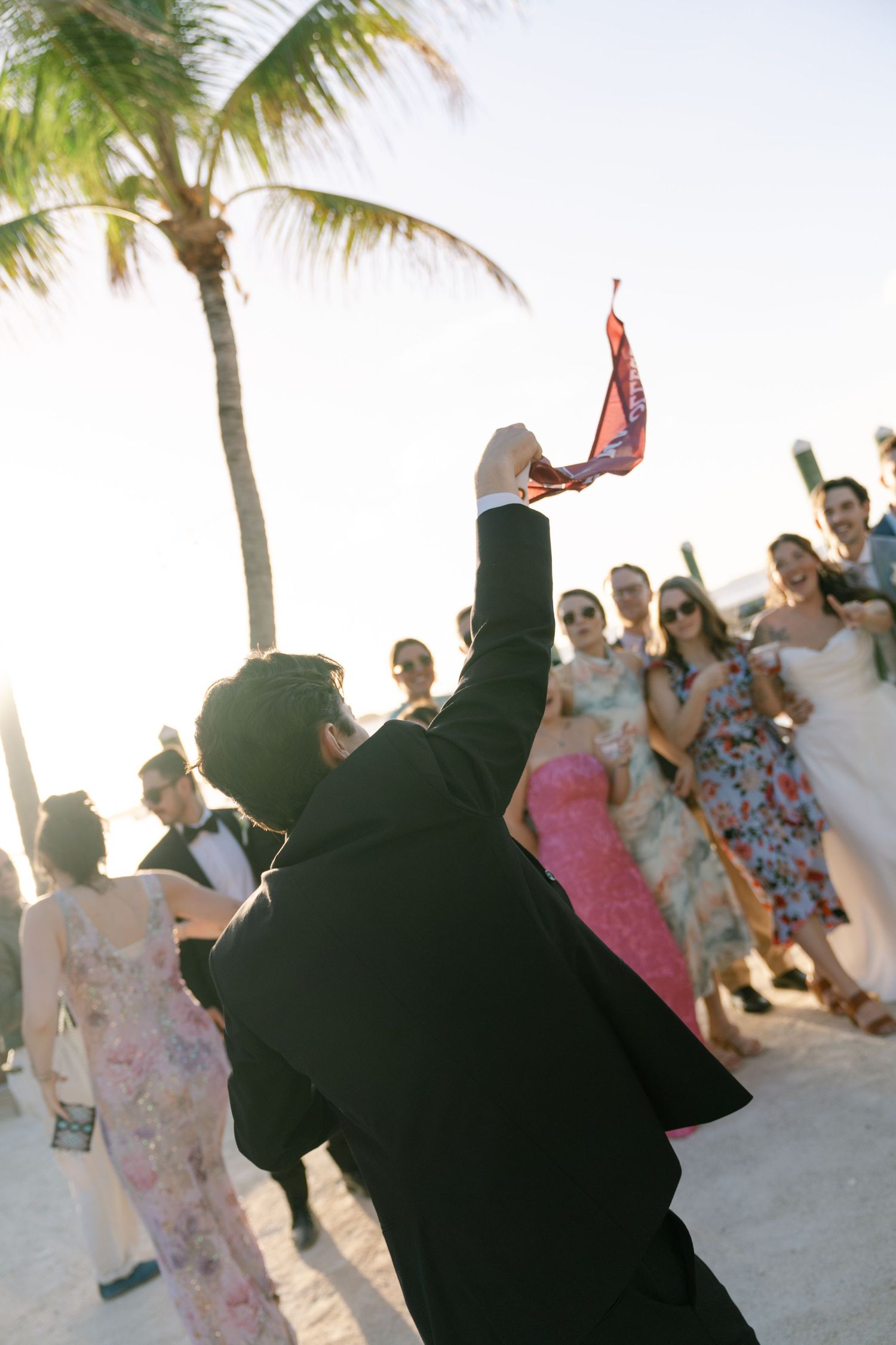 A group of people dancing on a beach with palm trees in the background.