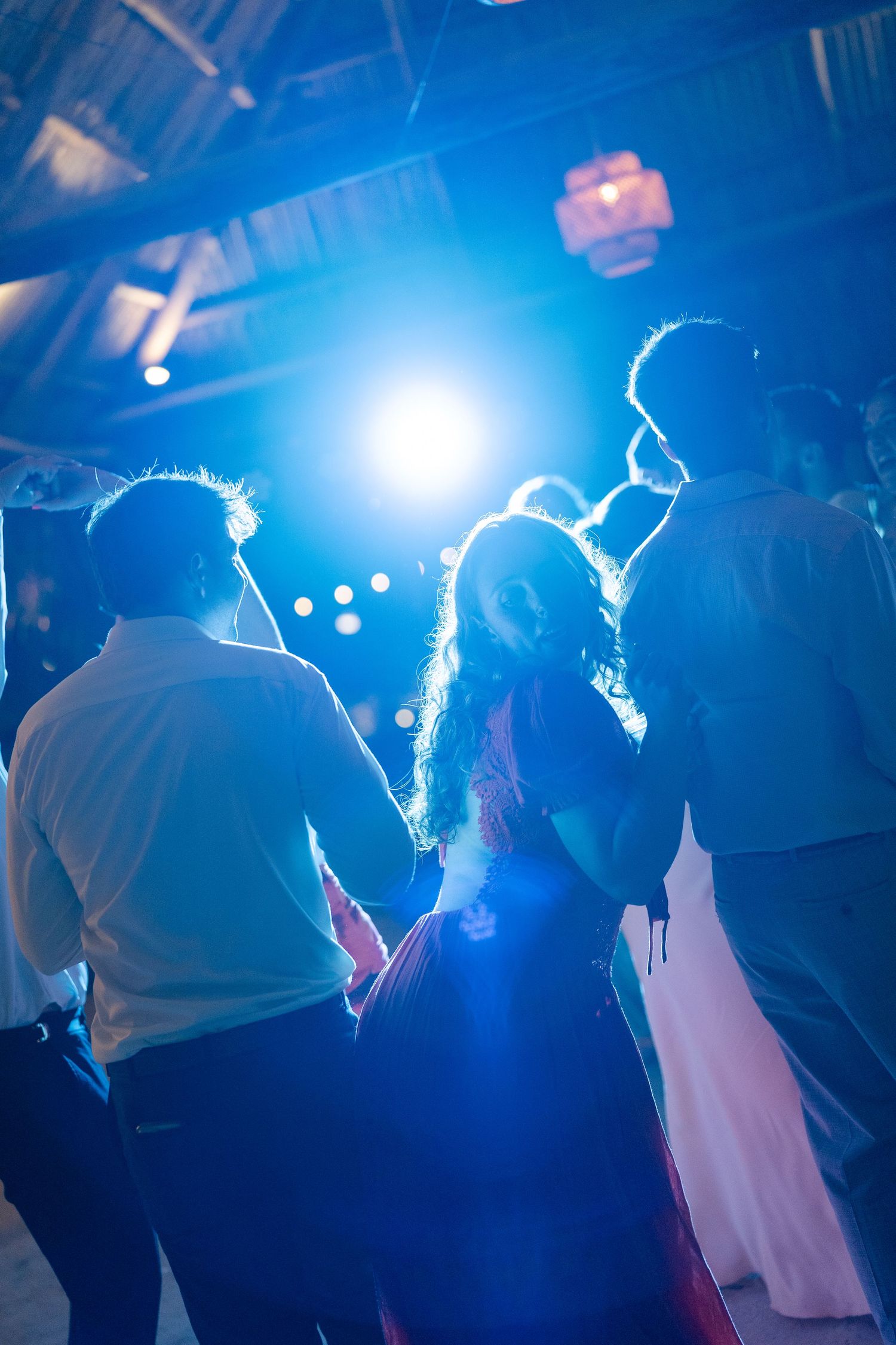 The image shows a crowd of people dancing at a lively event, with bright blue lighting illuminating the scene.