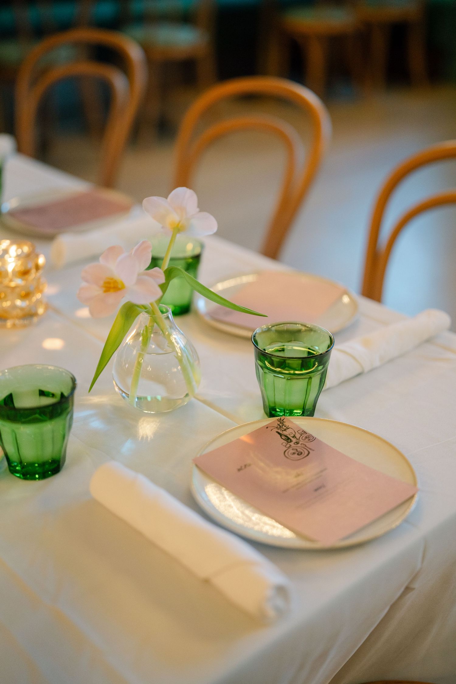 Elegant wedding reception table settings with white linens, green glassware and delicate floral accents.