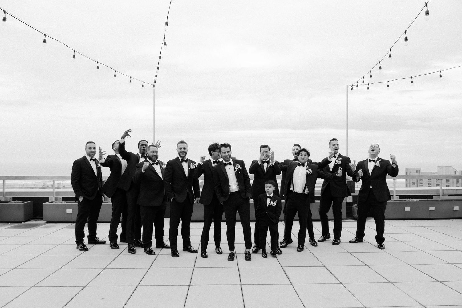 Large group of formally dressed people lined up on a rooftop for a panoramic wedding photo.