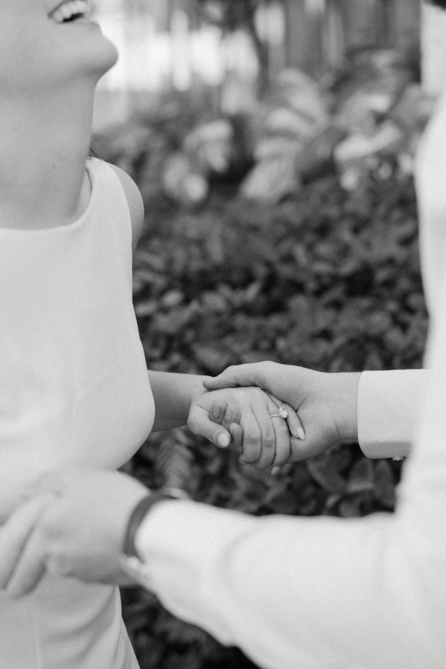 Black and white close-up of hands holding each other with wedding rings in a romantic gesture.