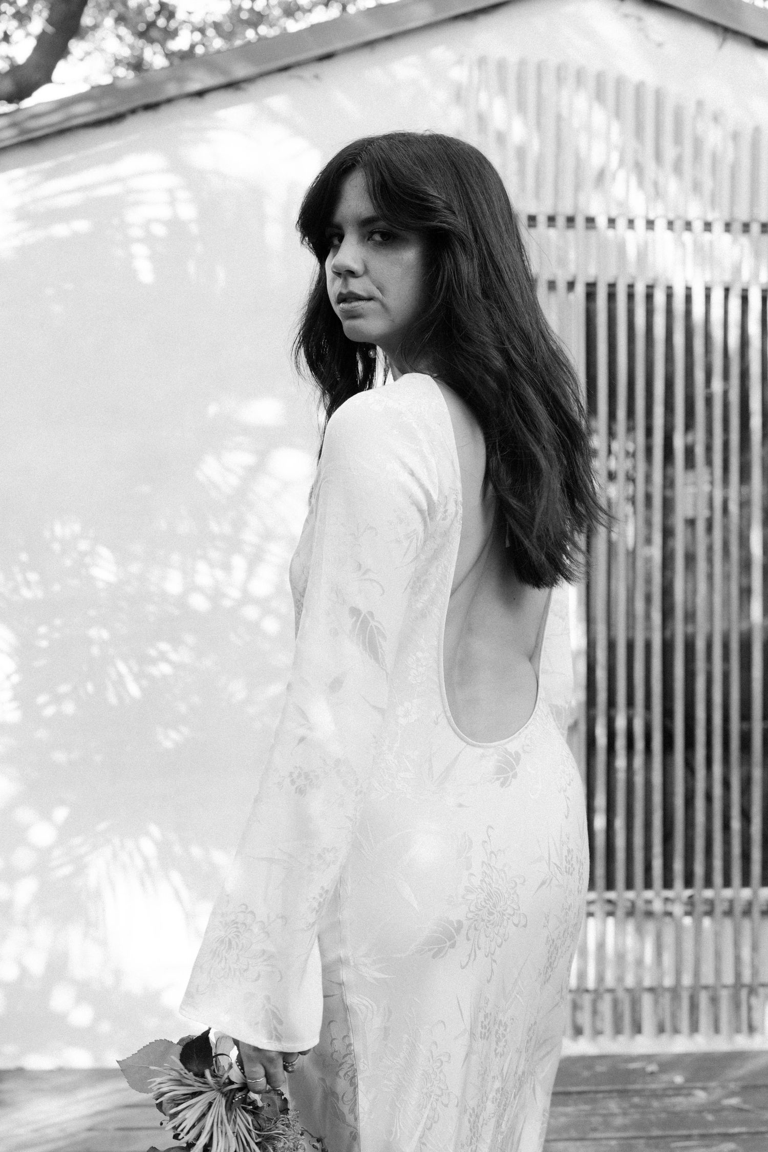 Ethereal portrait in white dress against sunlit garden fence.