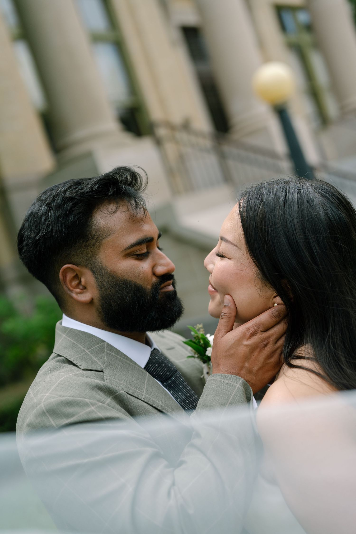 A groom tenderly holds his bride's face during an intimate wedding portrait outside a classic building.