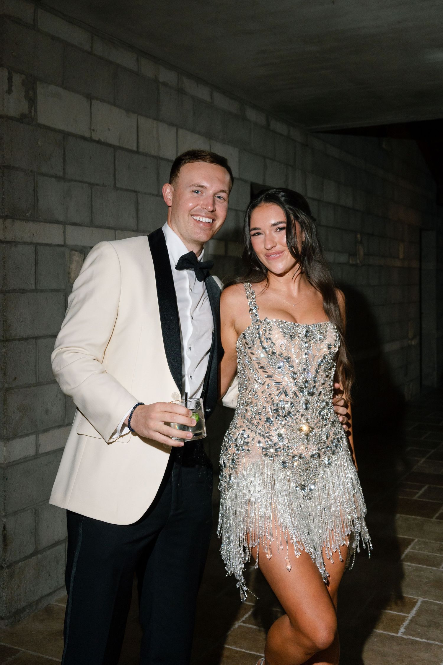 Couple posing together at wedding reception, groom in white tuxedo, bride in sparkly fringe dress.
