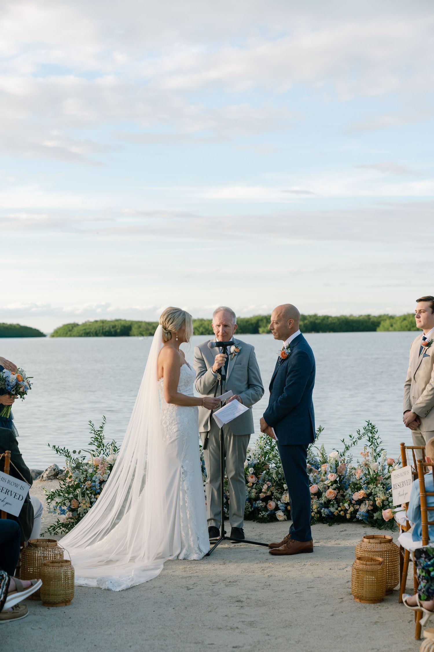 Oceanfront wedding ceremony with floral arrangements and wooden barrels as decor.