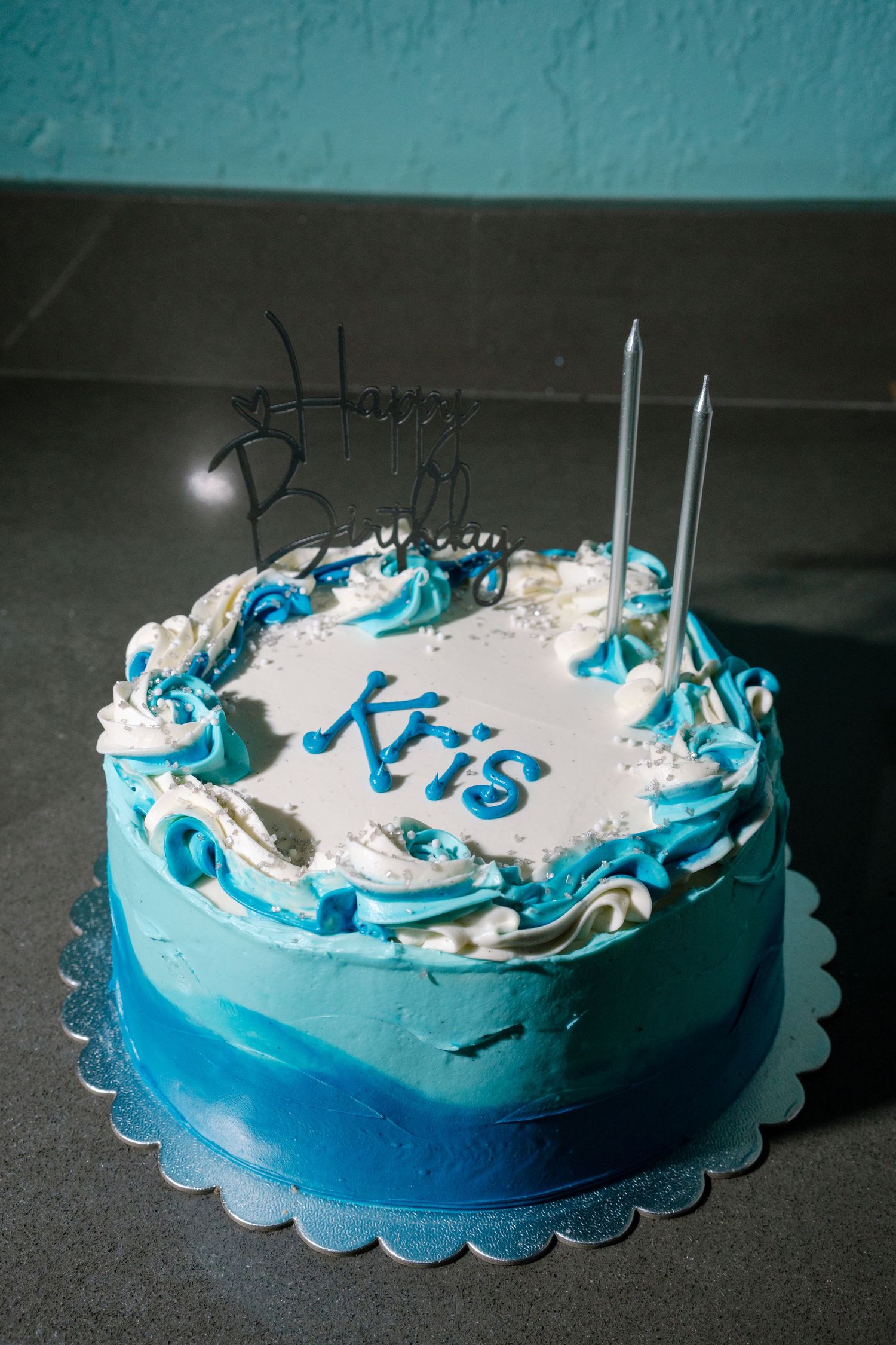 Blue and white decorated celebration cake with candles on a dark background.