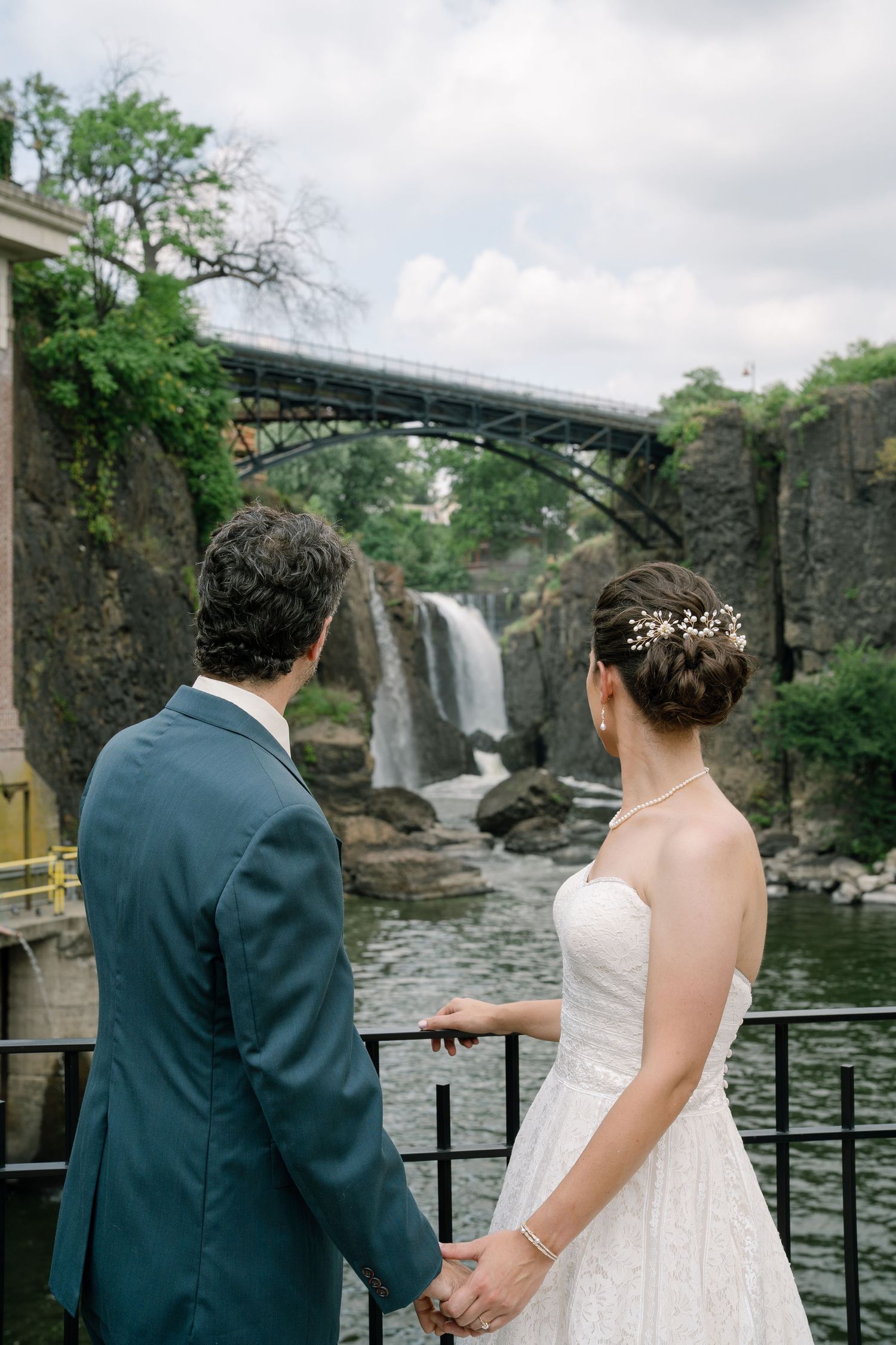 A romantic wedding photoshoot at a scenic waterfall with stone architecture and metal railings.