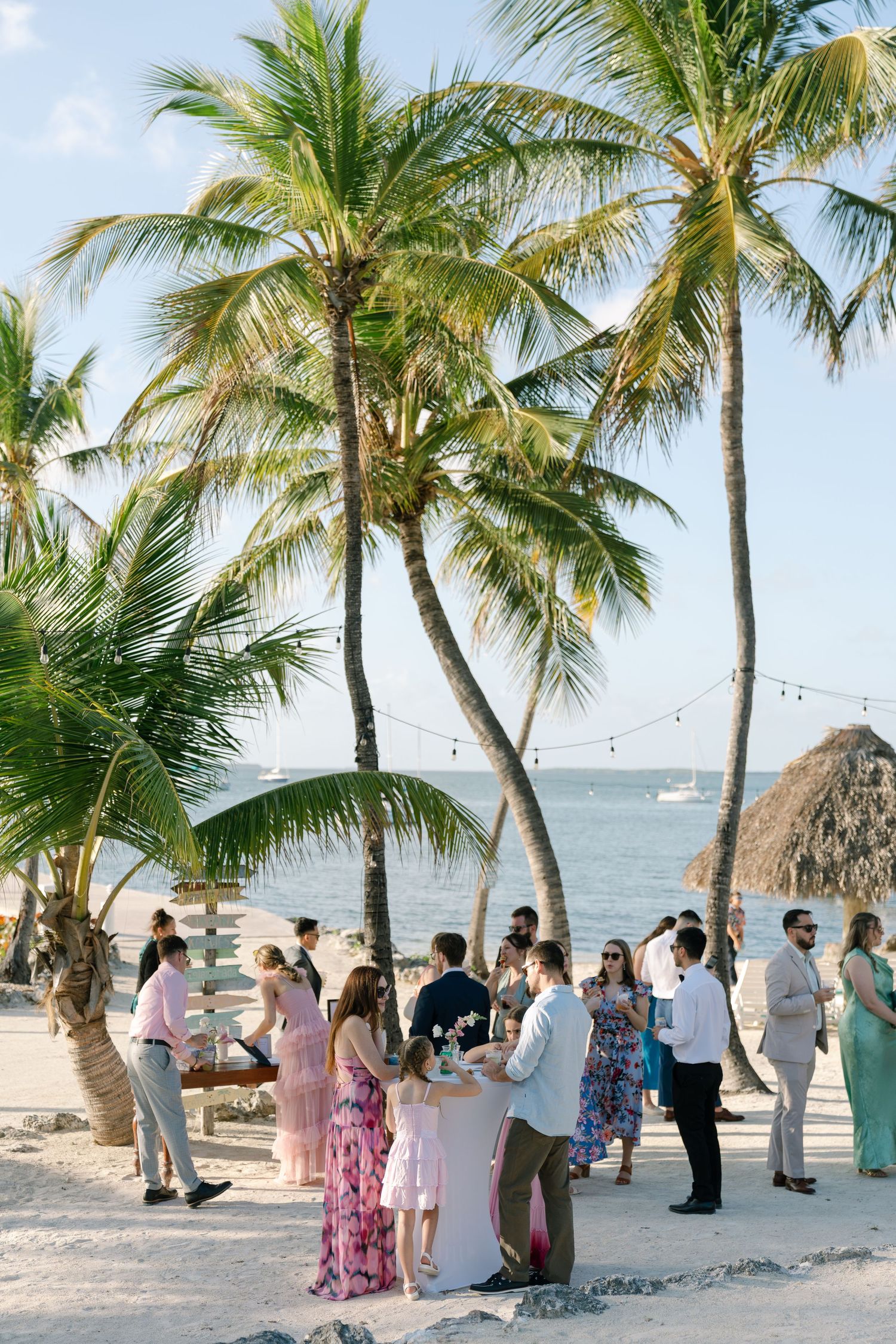A scenic tropical beach with palm trees and a group of people gathered for an event or celebration.