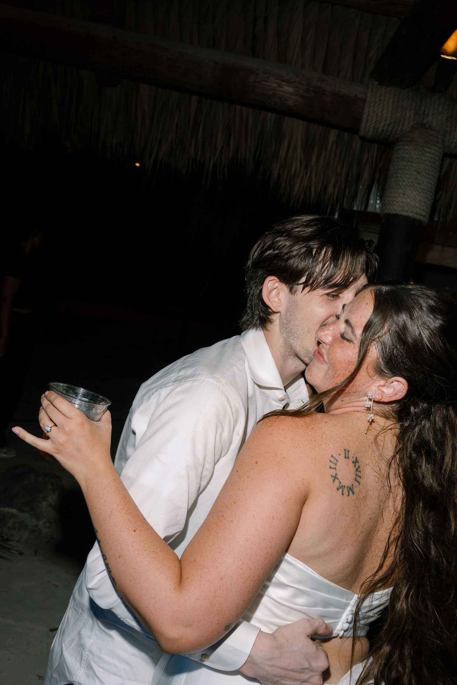 A couple embracing and kissing on a dimly lit dance floor, with other people in the background.