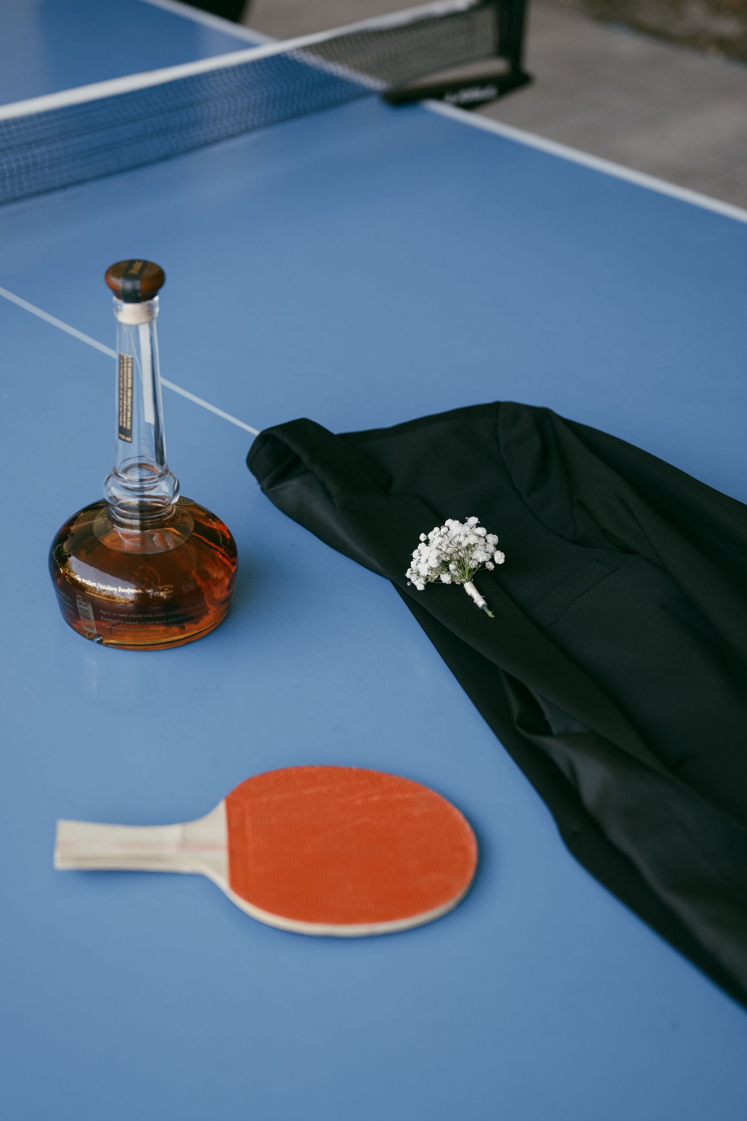 A row of orange ping pong paddles and sleek black cases arranged on a blue table surface with a clear glass decanter.