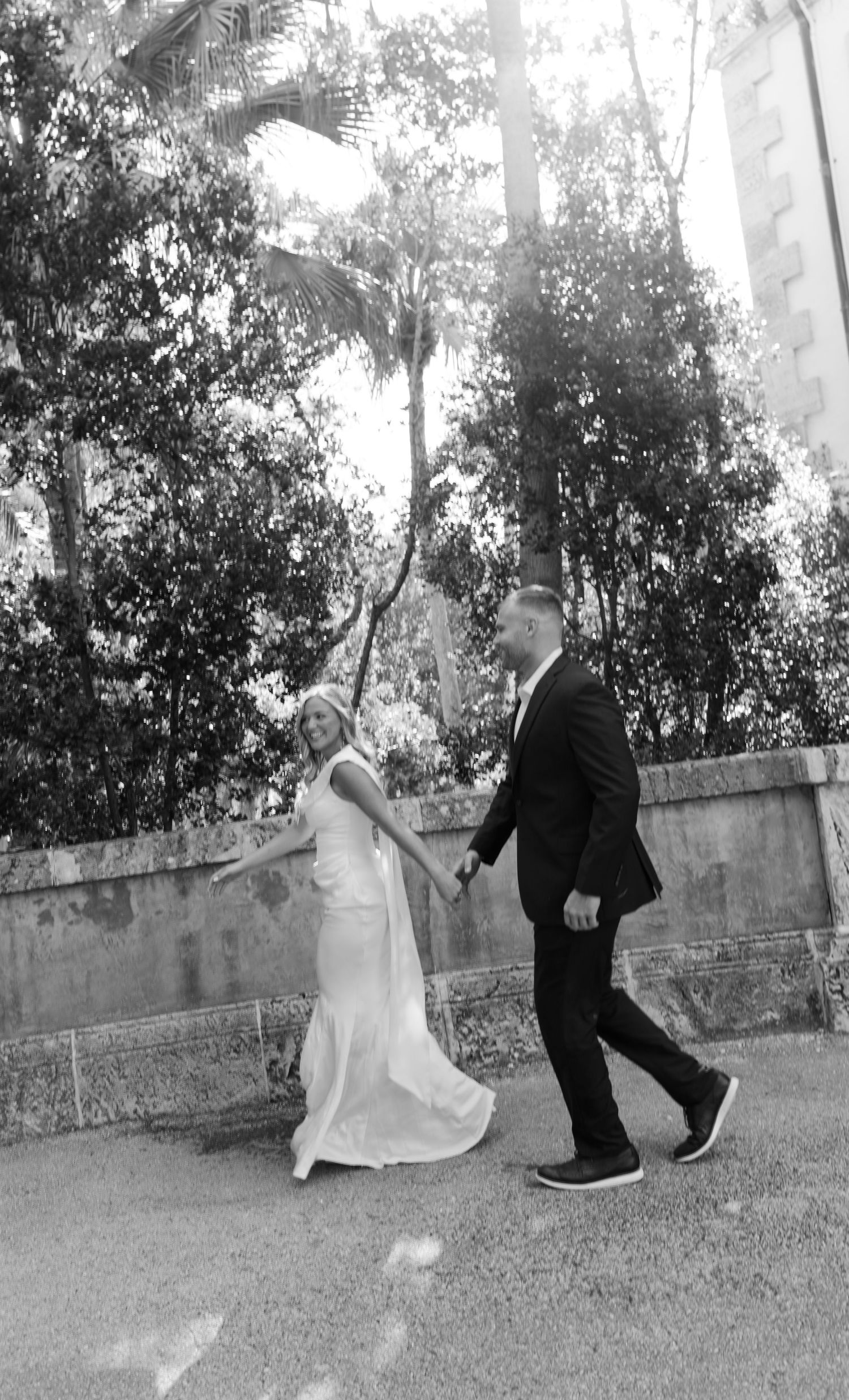 A vintage black and white wedding photo showing a couple walking together on a palm tree-lined path.