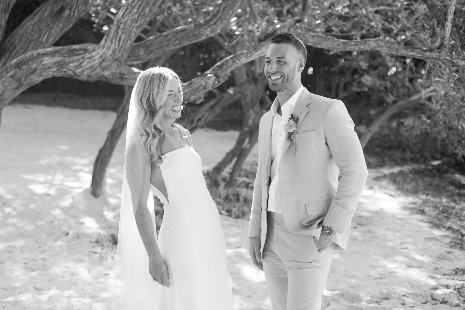A couple shares a joyful moment together during their beach wedding ceremony in black and white photography.
