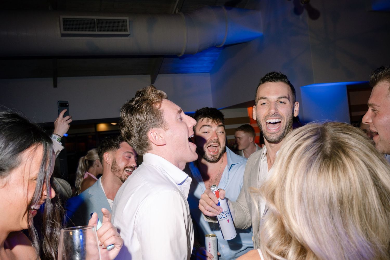 Lively reception party scene with guests celebrating under dim lighting.