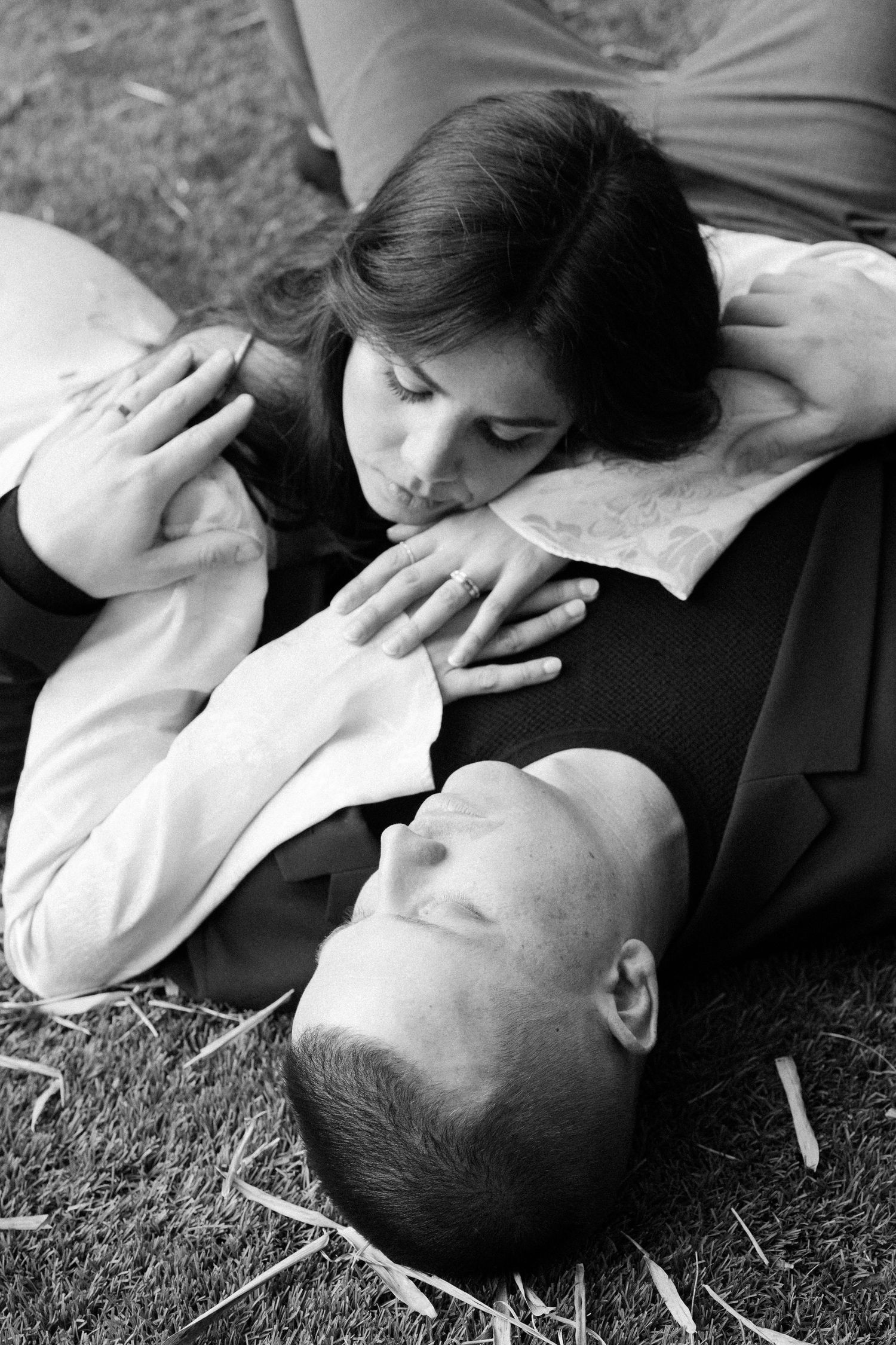 A tender black and white photo series showing a couple lying on grass in intimate, romantic poses.