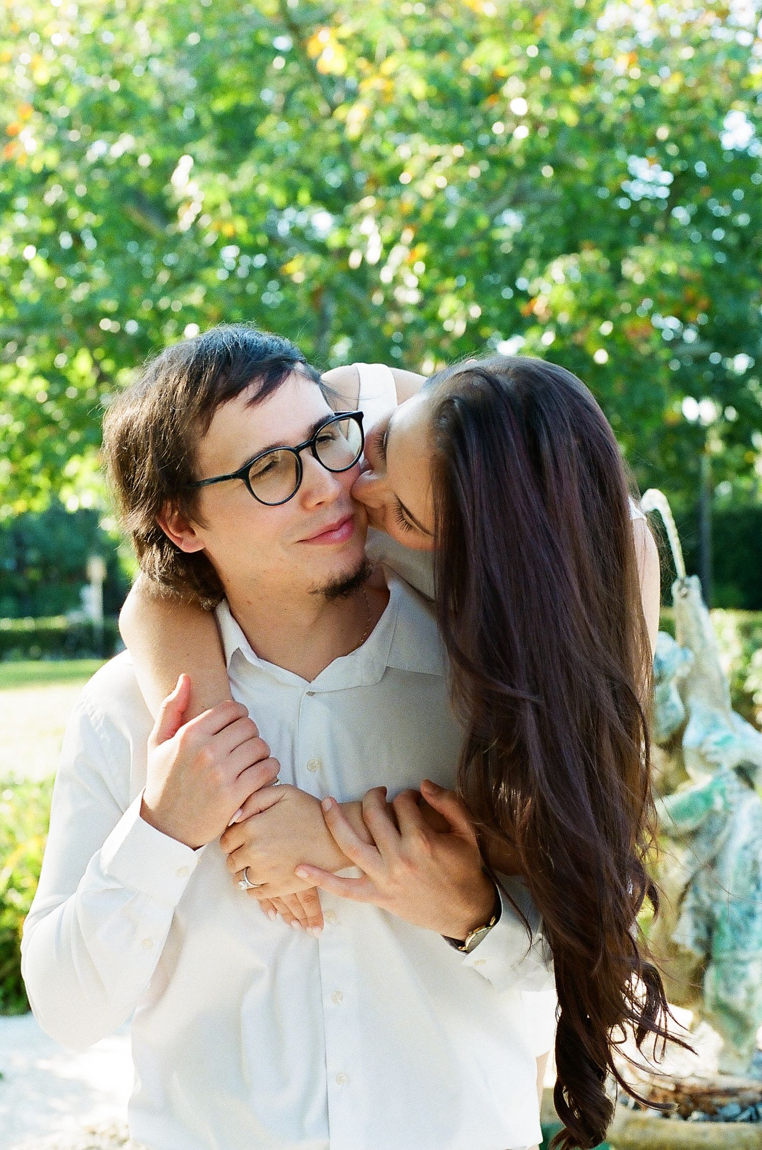 A romantic couple in white attire share tender moments in a sunny garden setting.