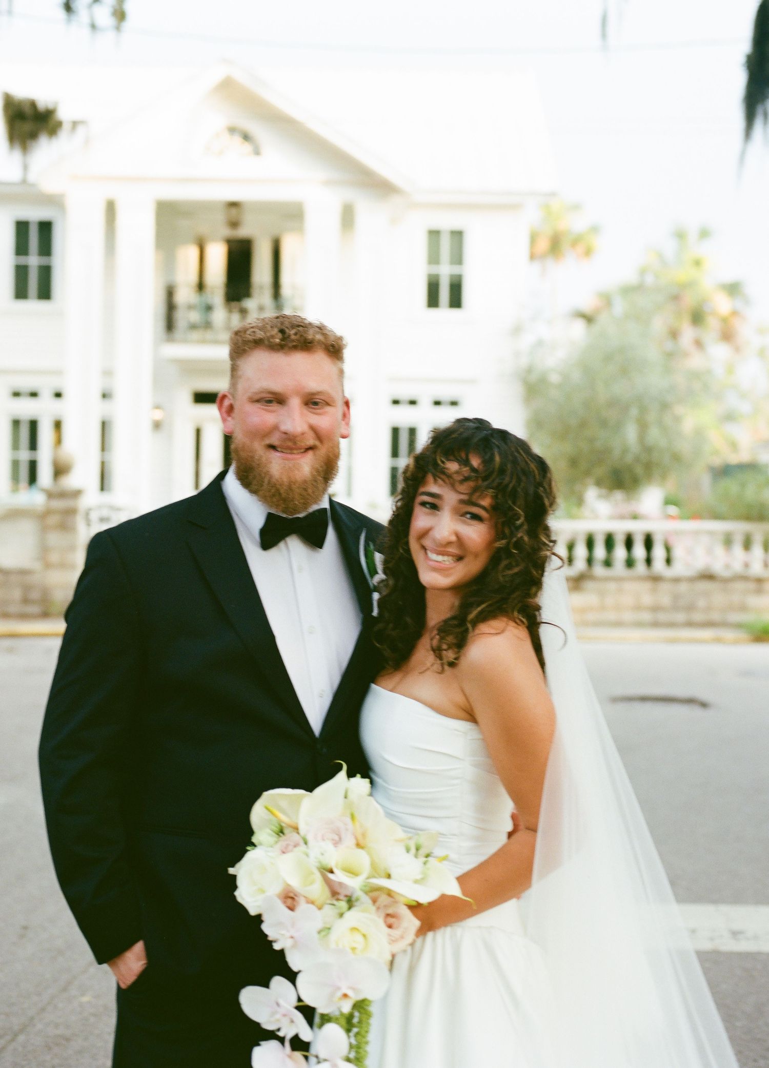 Wedding portrait of newlyweds in front of a classic white Southern mansion with columns.