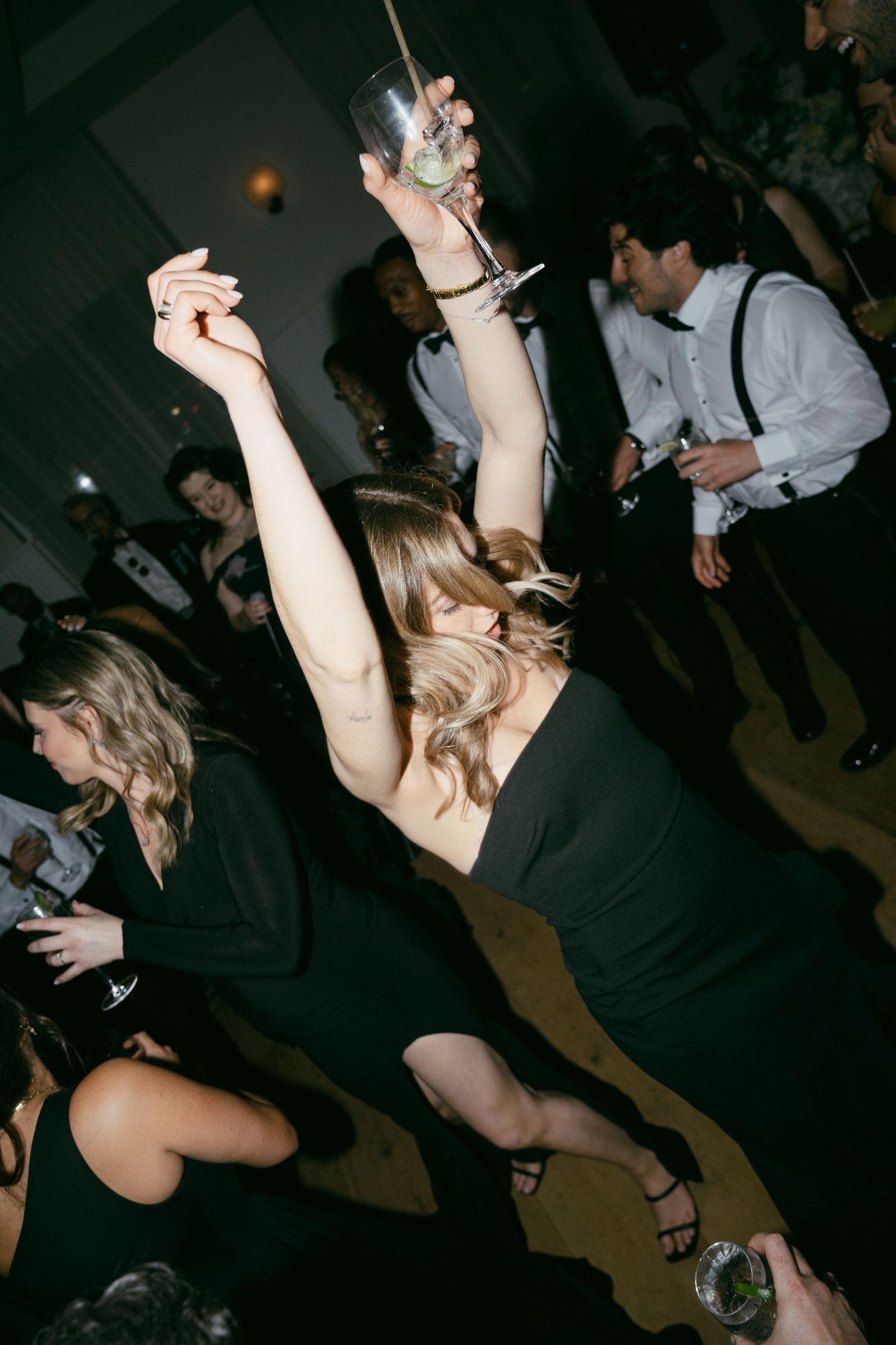 Wedding guests dancing energetically on a dimly lit dance floor during reception celebrations.