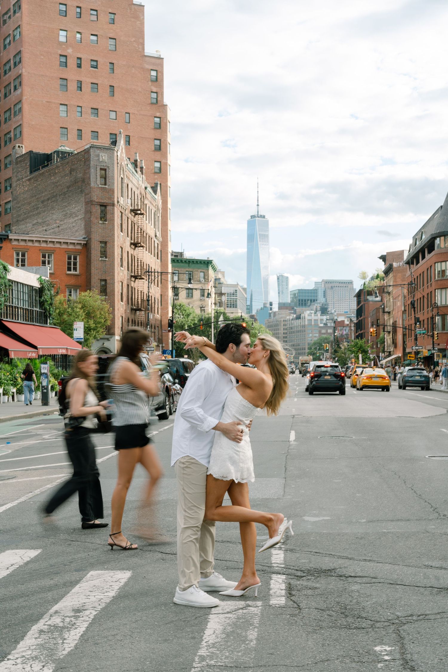 Couple embracing and kissing in NYC crosswalk with One World Trade Center skyline in background.