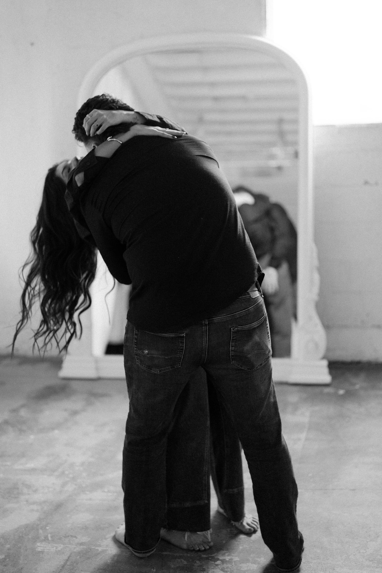 Black and white photo of a couple embracing in an intimate dance pose with window light in background.