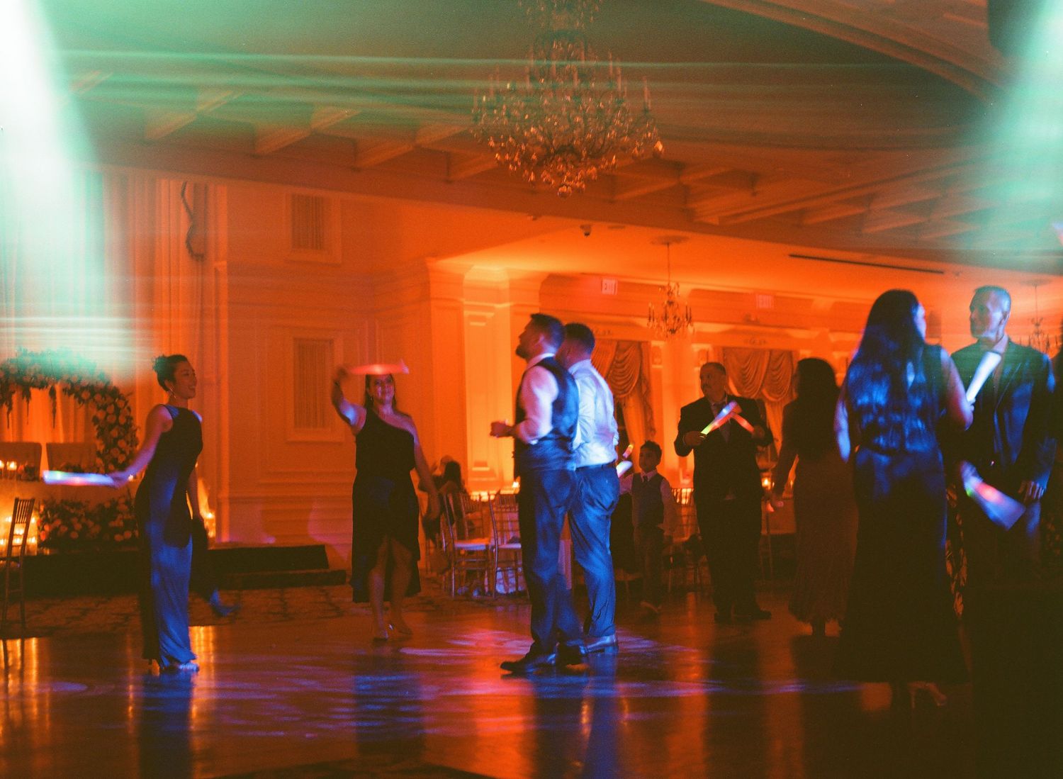 Couples slow dance under soft blue and orange lighting at an elegant ballroom reception event.
