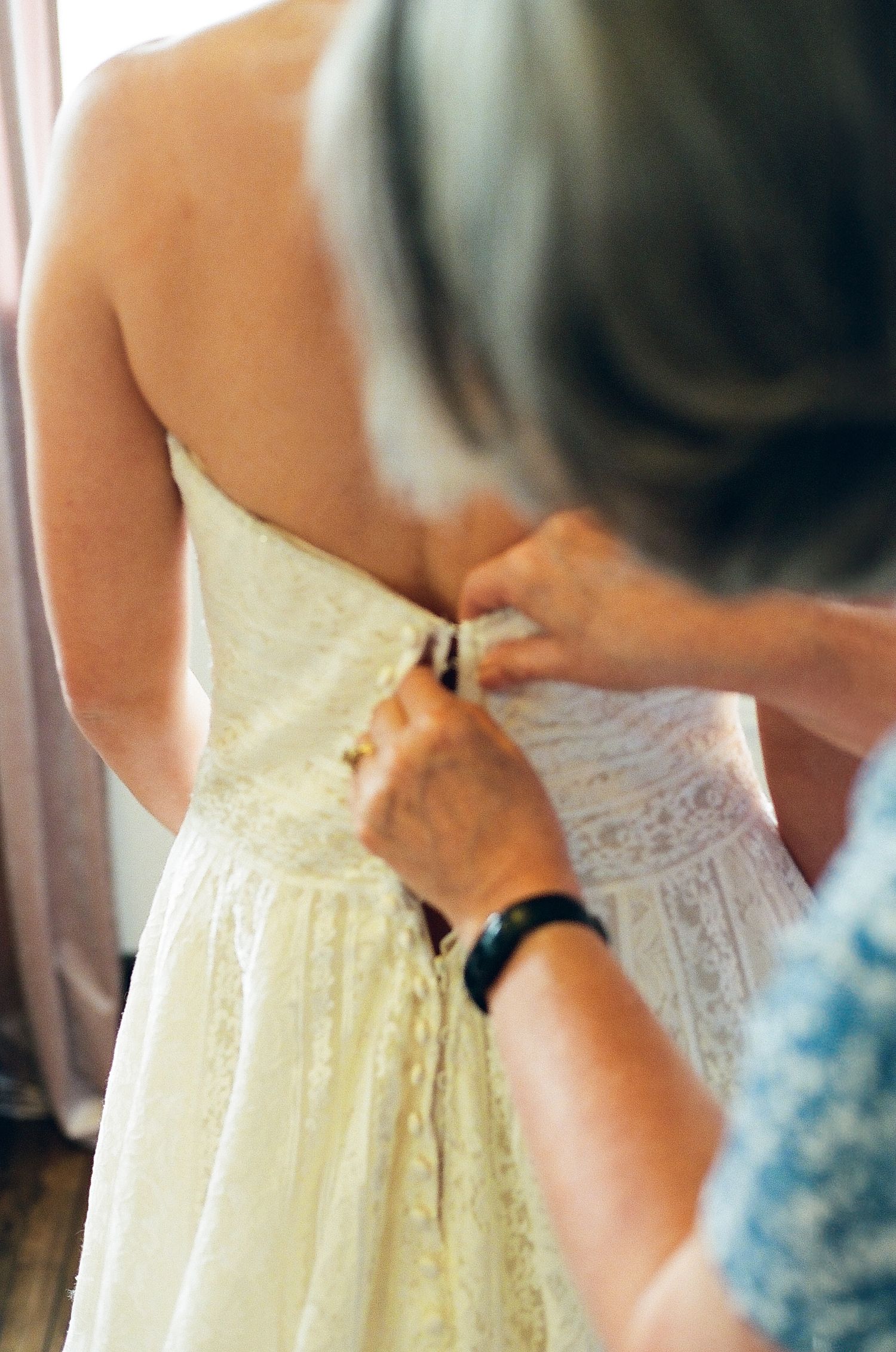 Close-up view of someone adjusting the back of an elegant cream-colored wedding dress with intricate lace details.