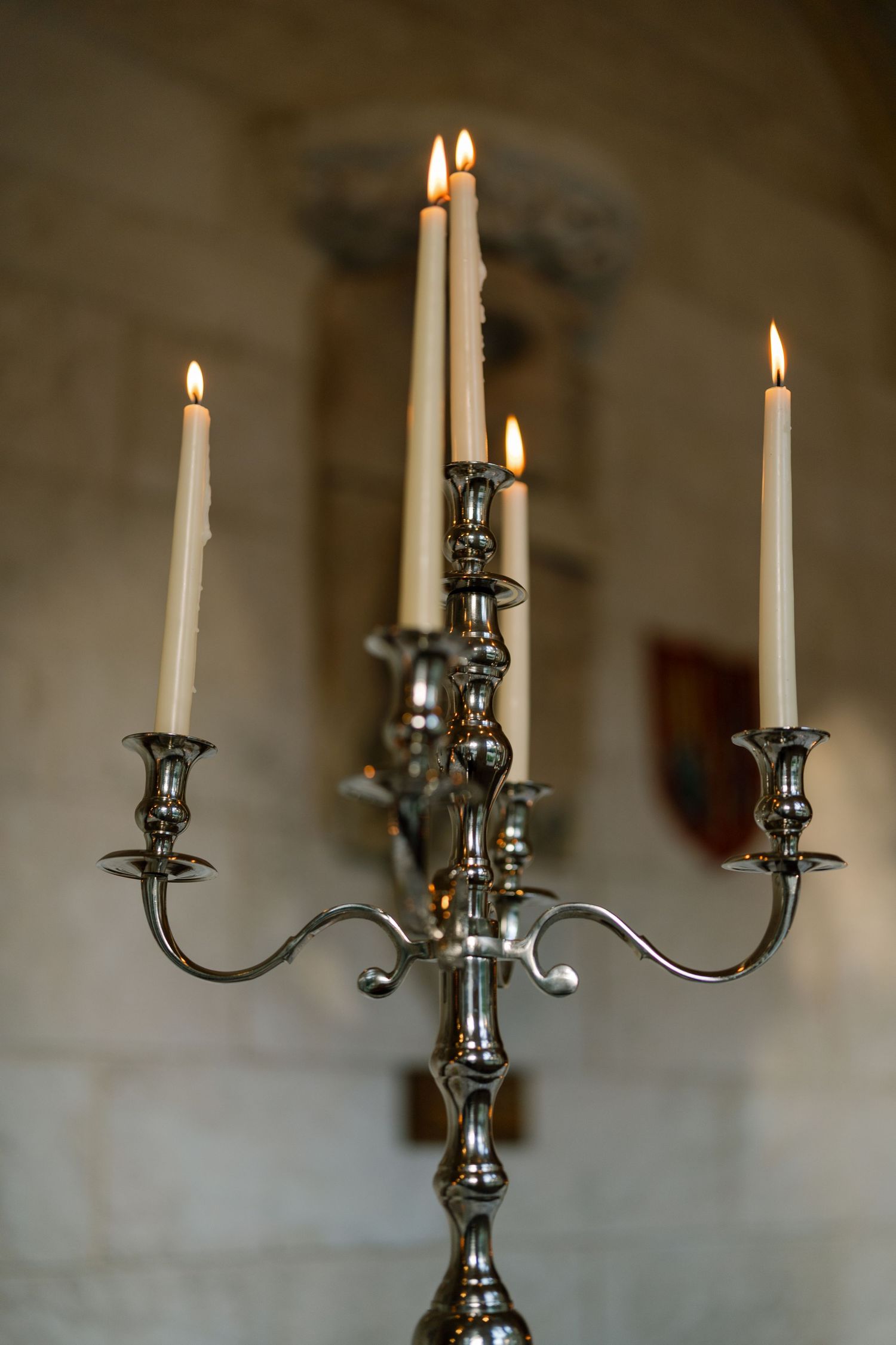 Silver candelabra with five lit white candles glowing in a stone church interior.