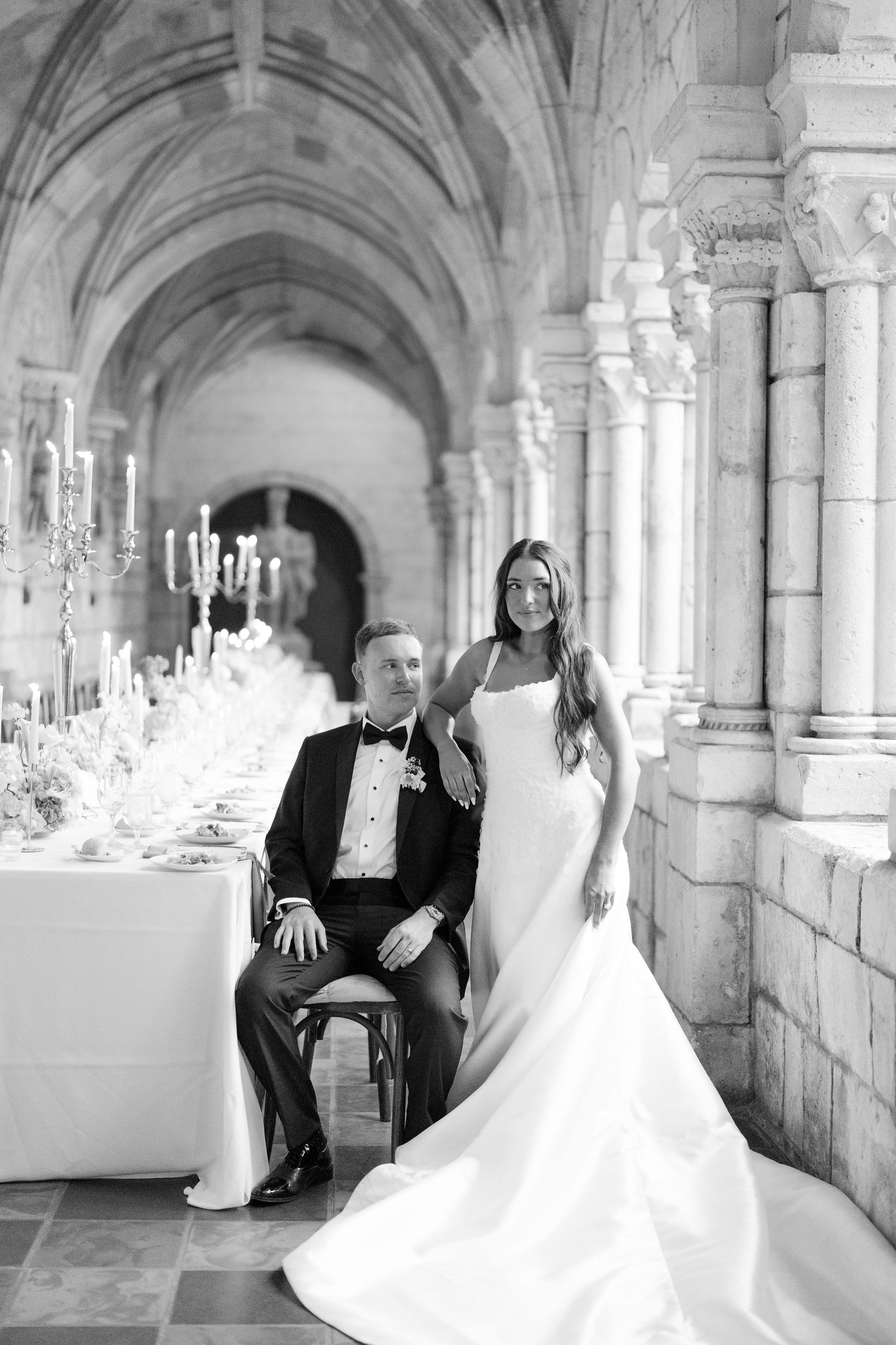 A black and white portrait of a bride and groom posing in an elegant stone cathedral reception hall.
