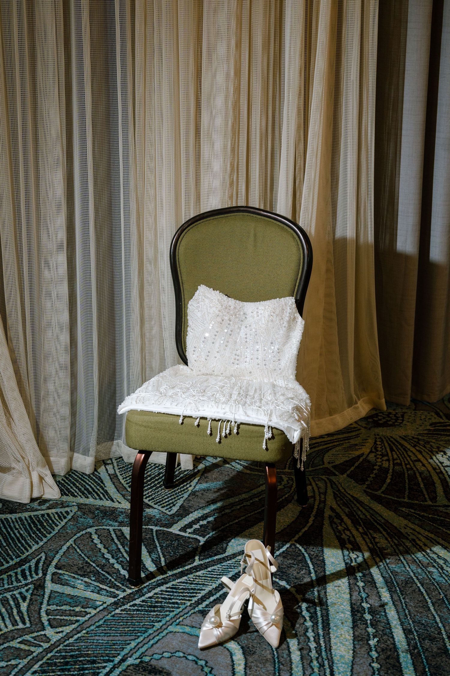 A sequence of chairs with white cushions on olive green upholstery against a curtained wall with geometric carpet below.