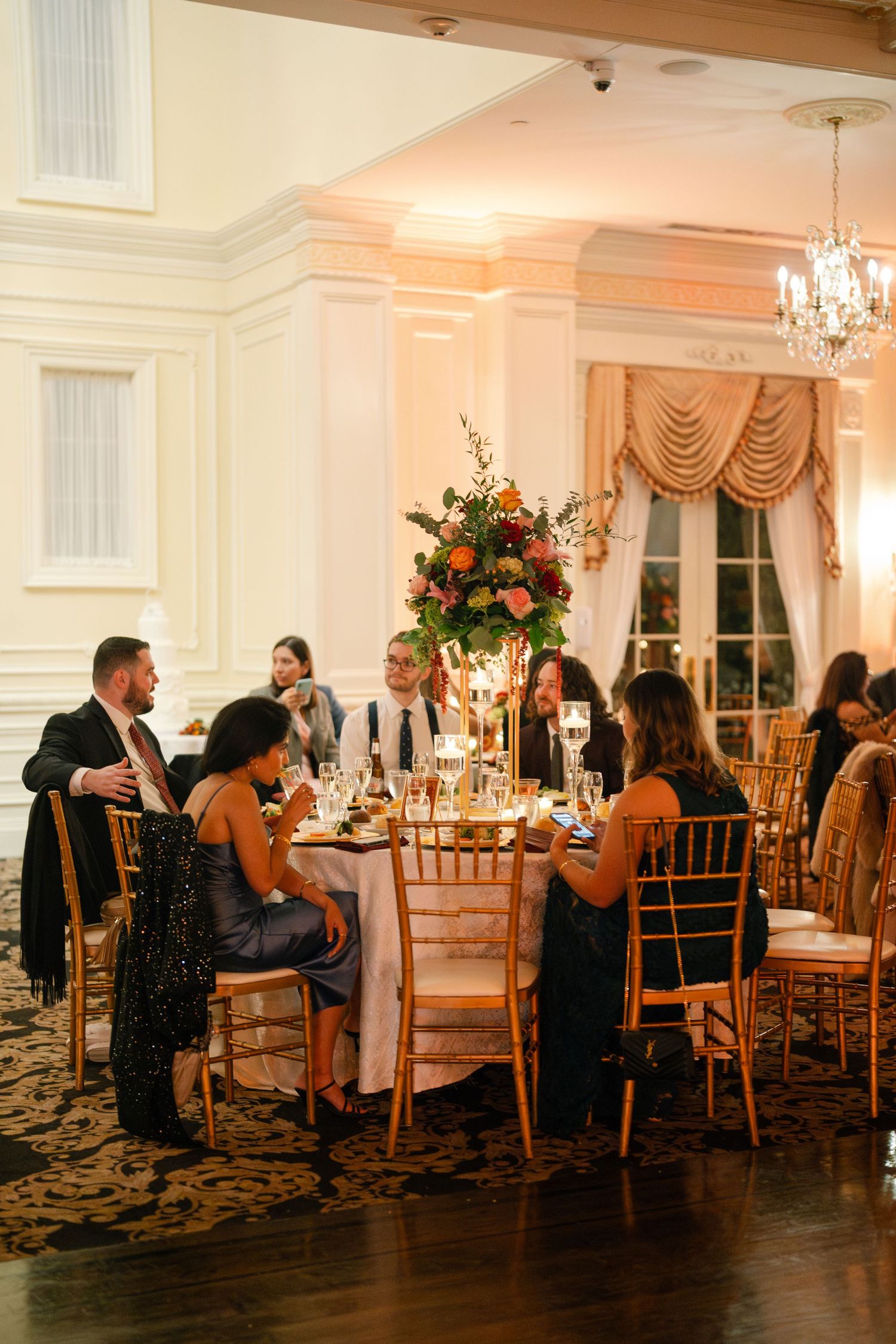 Elegant reception hall with crystal chandeliers and coral floral centerpieces.