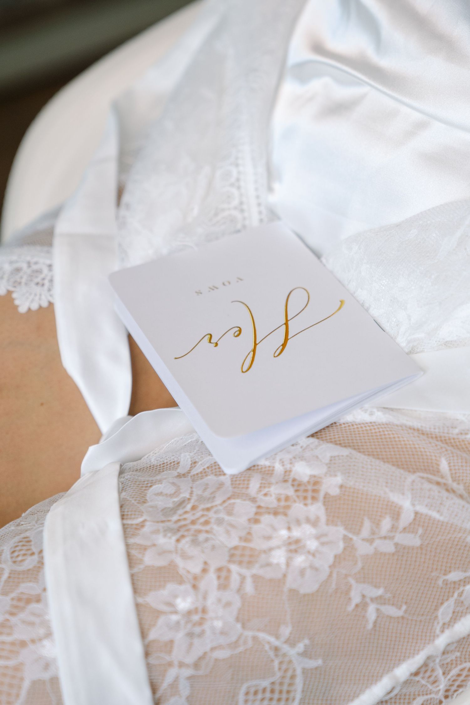 Delicate white lace wedding details and stationery with elegant gold calligraphy laid out on a light surface.