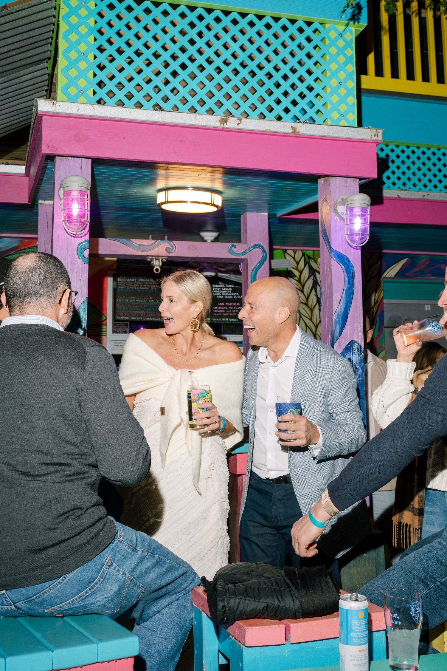 People enjoying drinks at a colorful tropical-themed bar with turquoise lattice decor.