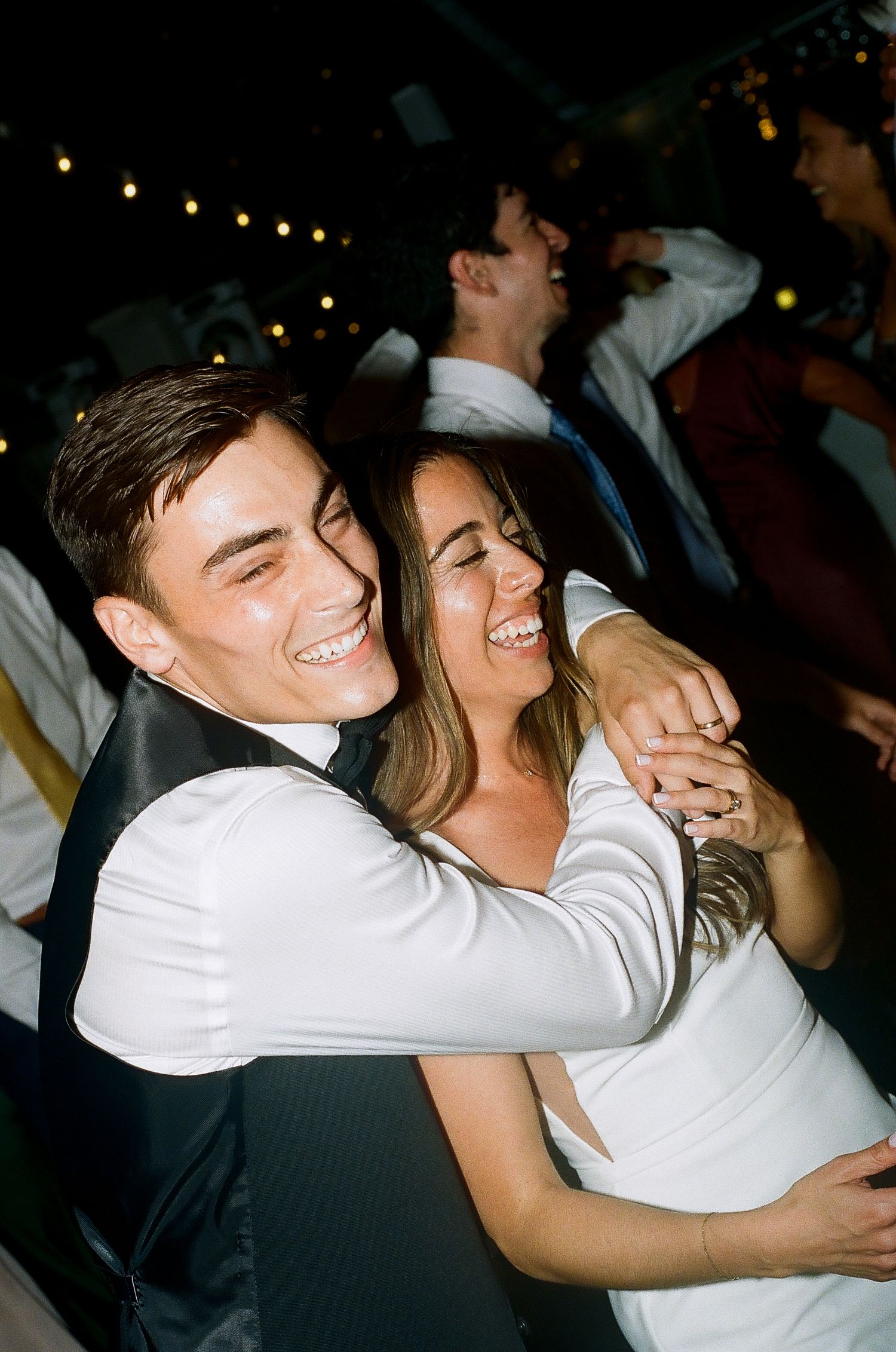 Joyful bride and groom embrace and laugh together on the dance floor during their wedding reception at night.
