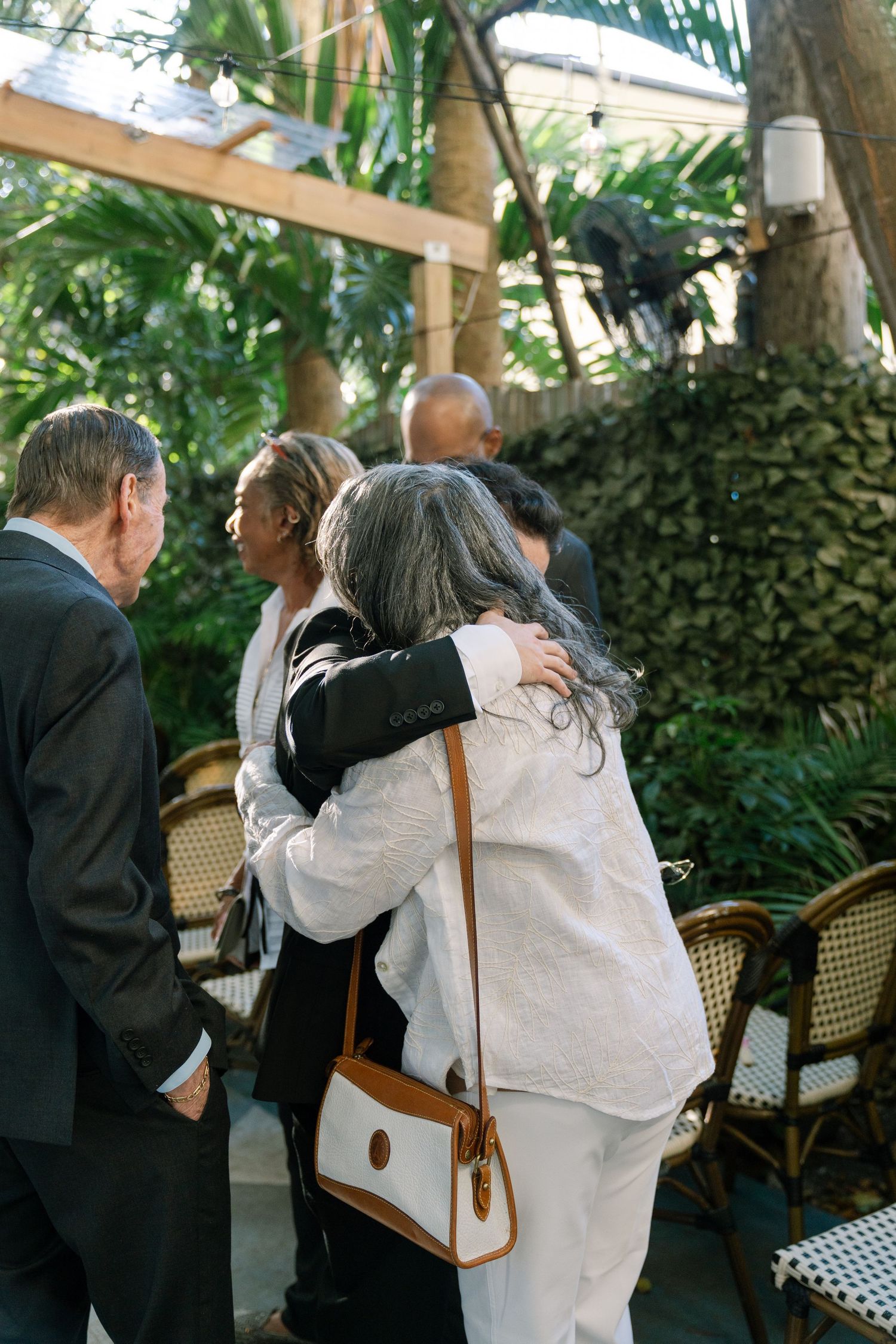 Guests embracing at an outdoor wedding ceremony surrounded by lush tropical greenery.