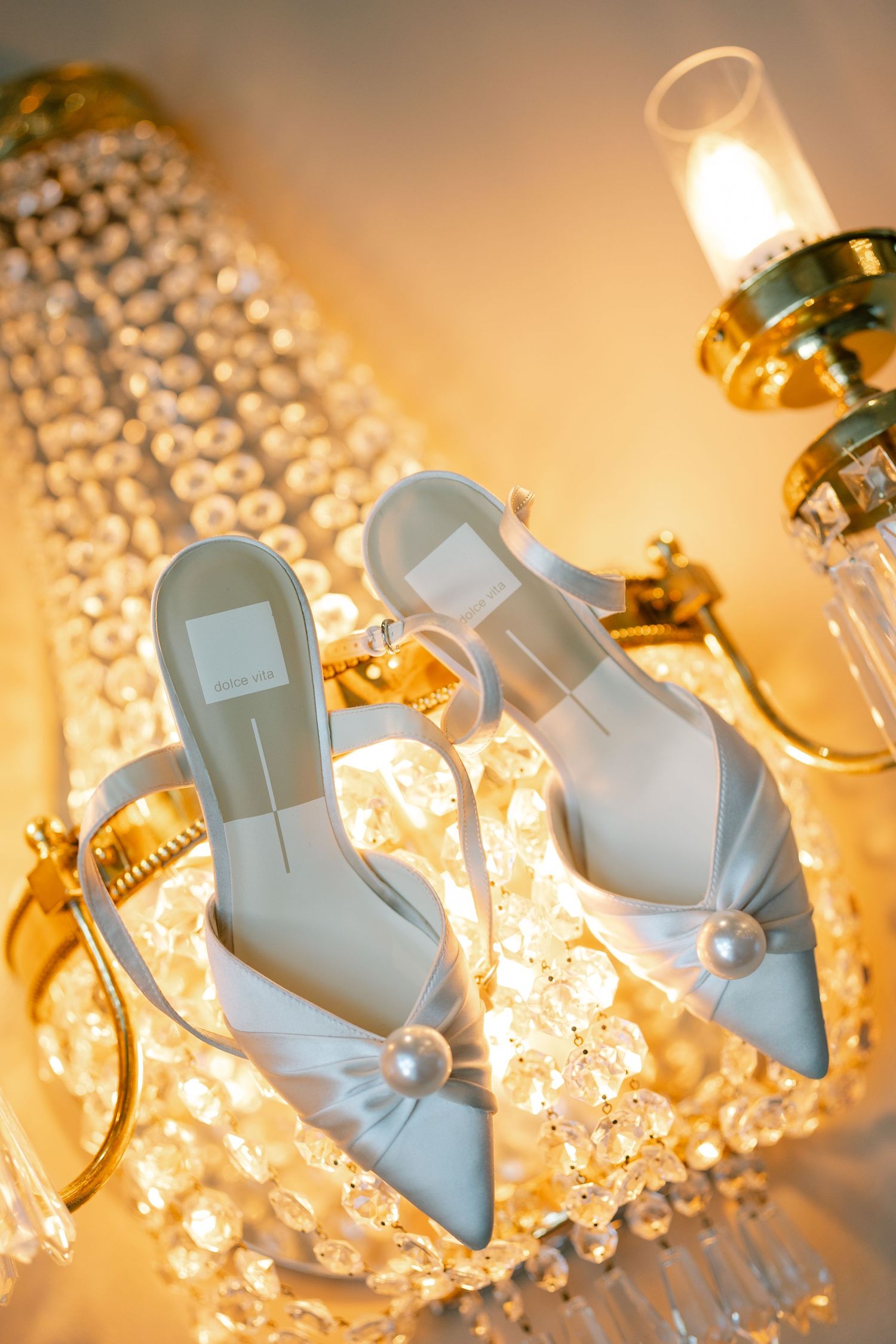 Elegant light blue bridal shoes with pearl details displayed against a crystal chandelier backdrop.