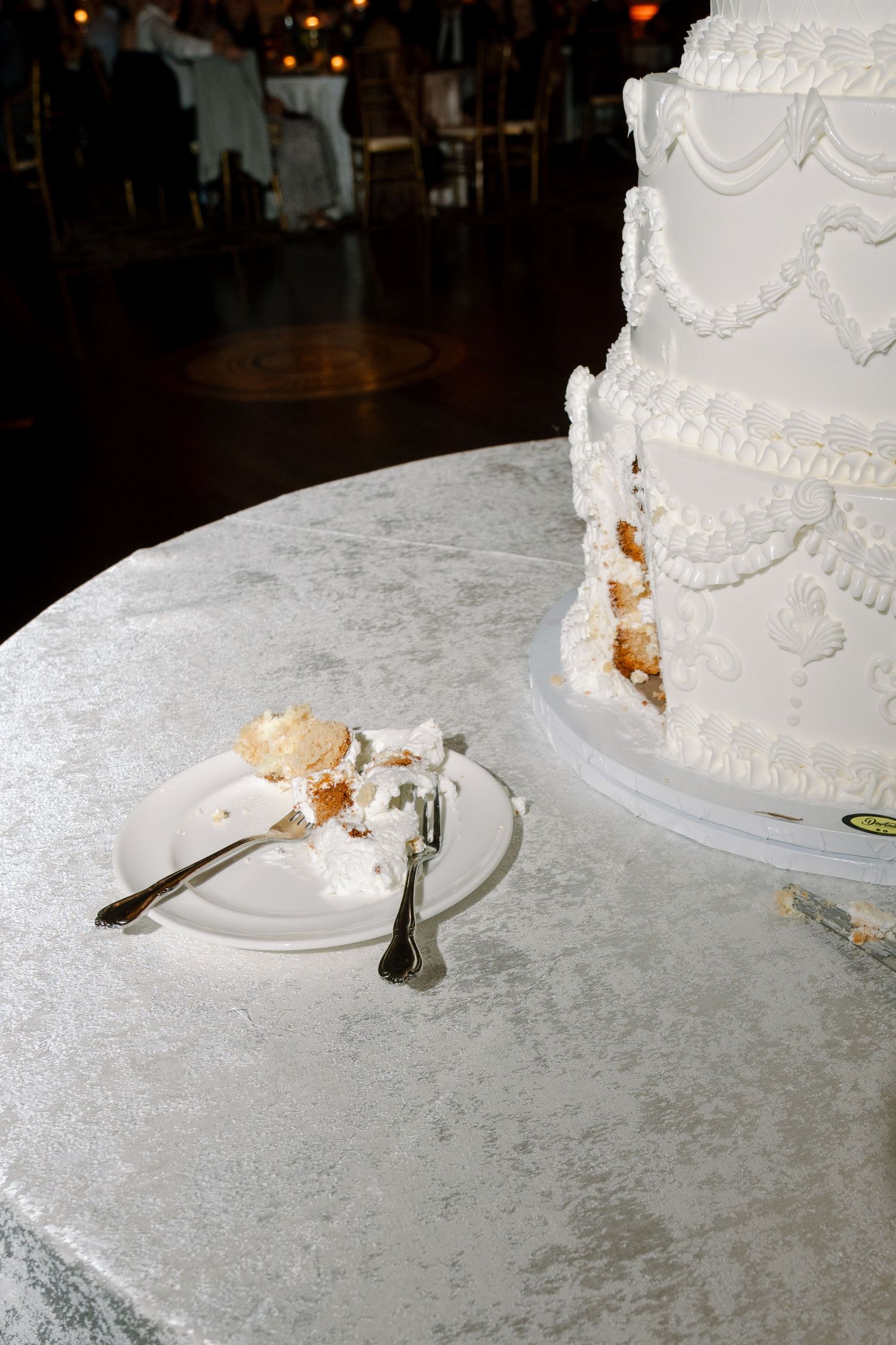 White wedding cake with intricate piping detail on silver tablecloth.