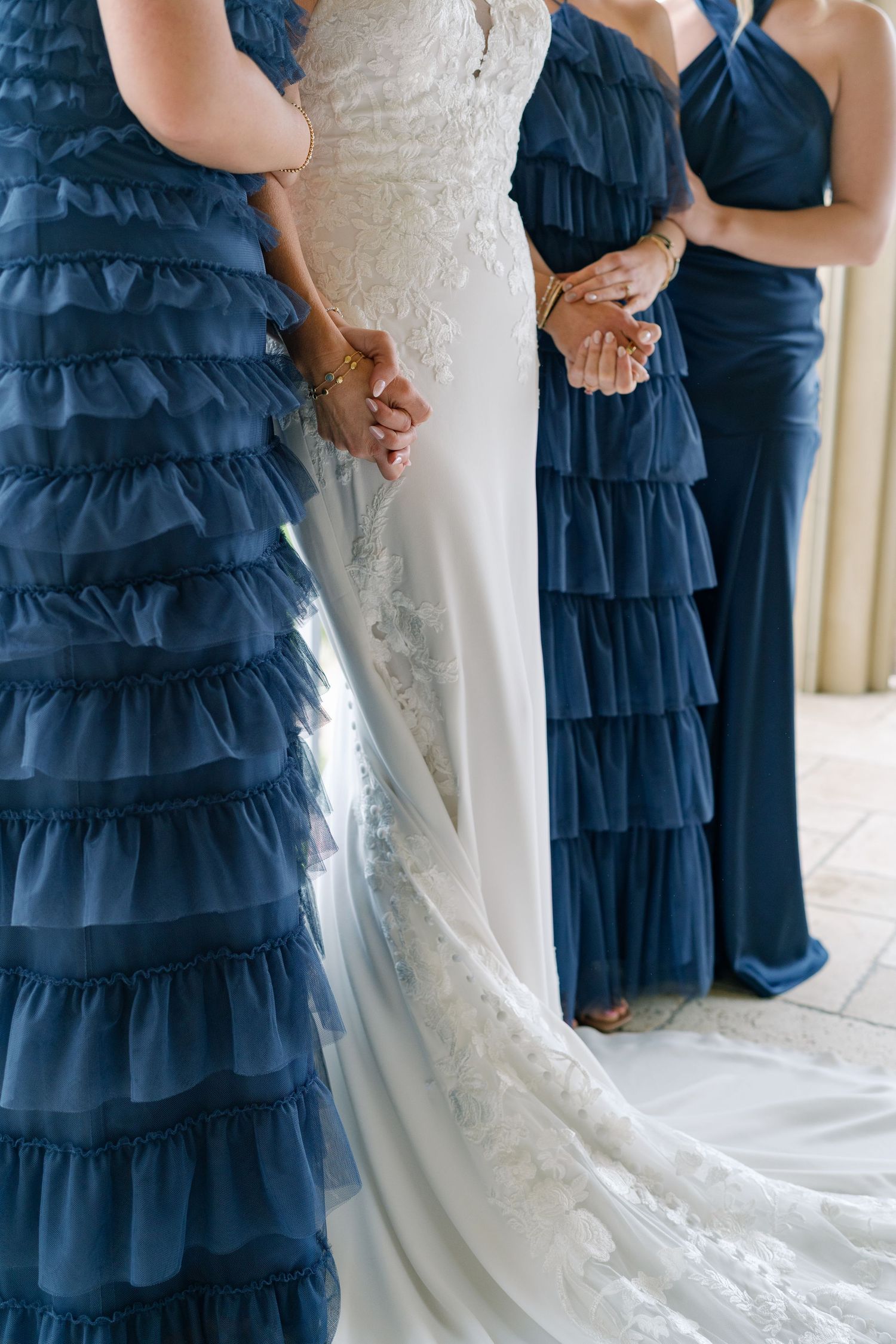 Wedding party detail showing navy blue tiered bridesmaid dresses next to white lace bridal gown.