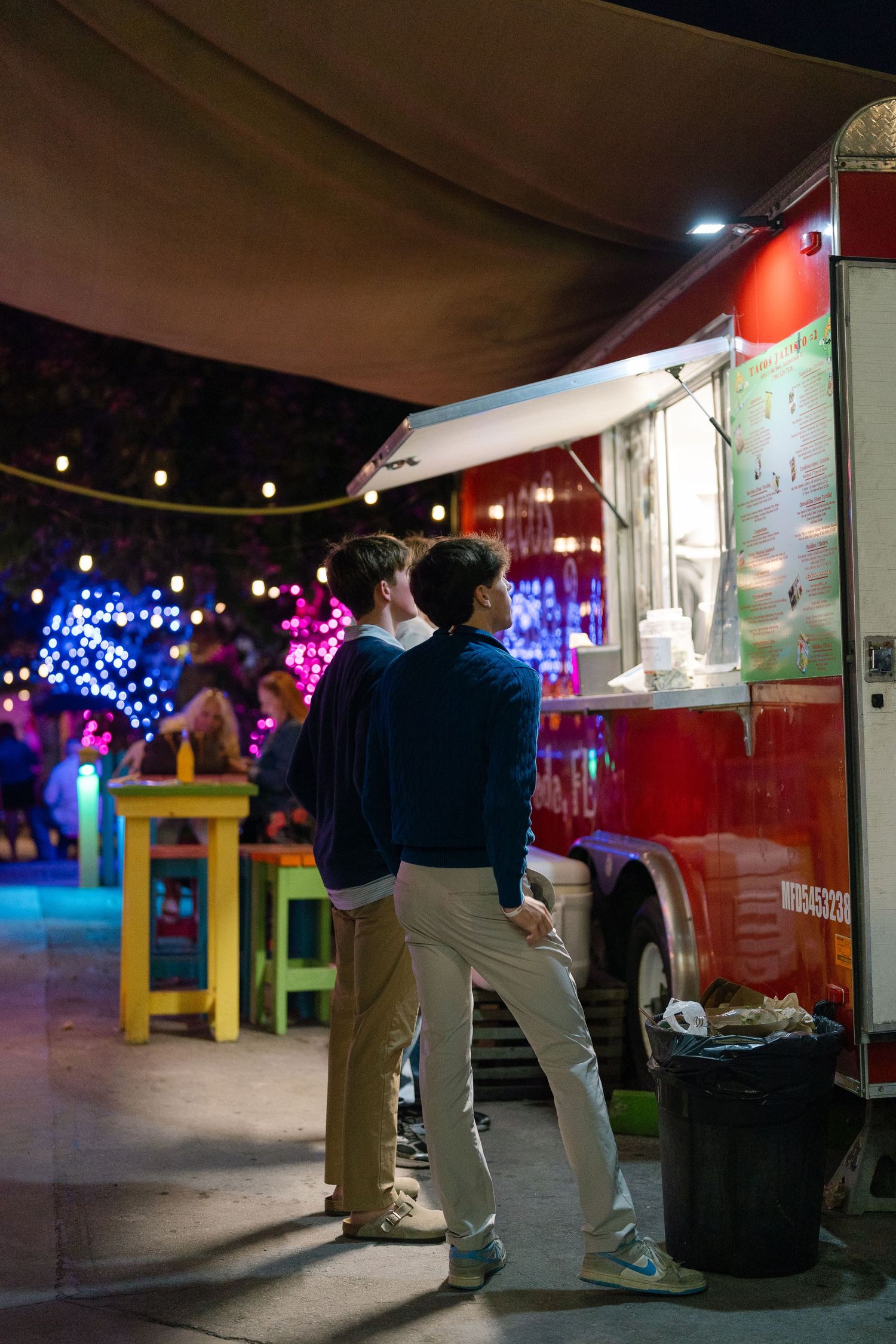 People dancing at night with colorful lights and food stalls creating a festive outdoor atmosphere.