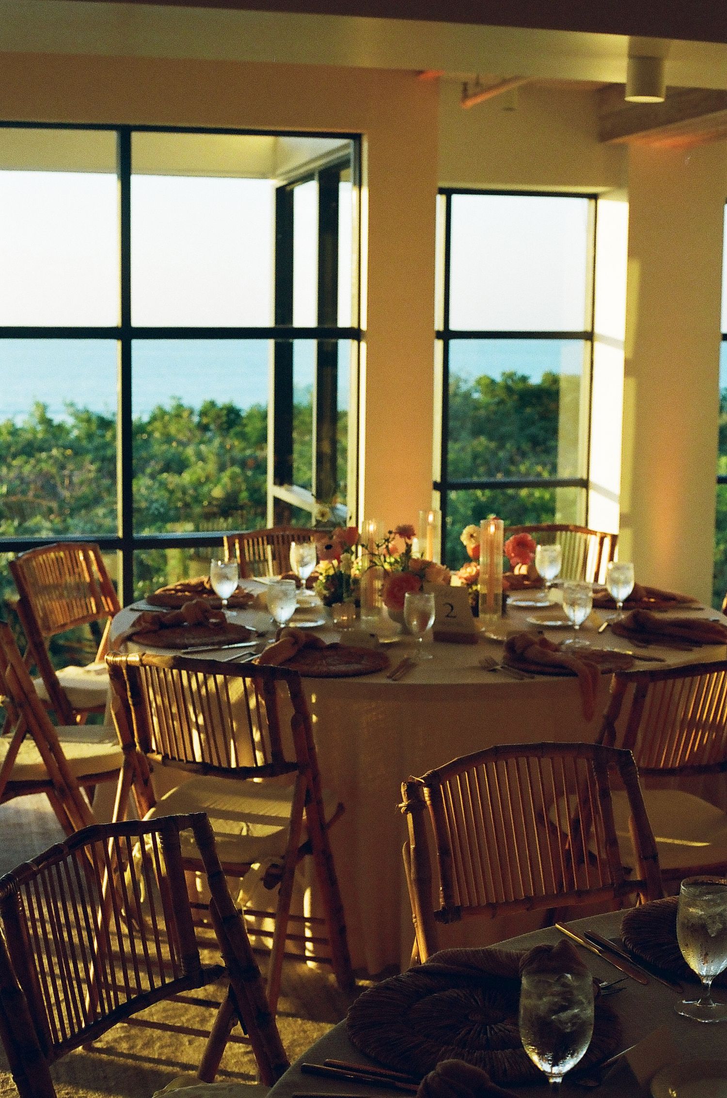Wedding reception venue with wooden chairs and elegant table settings bathed in warm natural light.